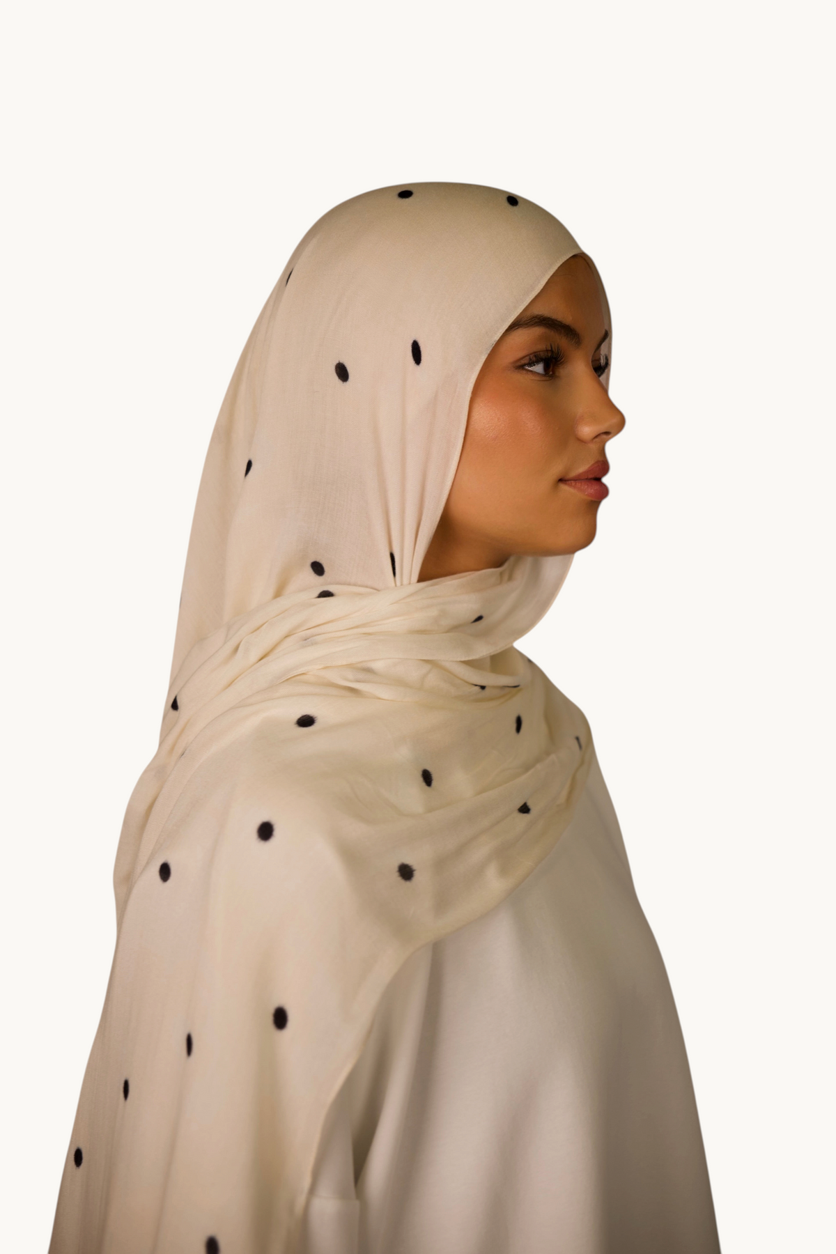 LOSYANA leichter Modal Hijab in Creme mit schwarzen Velour-Punkten, getragen von einem Model im Profil