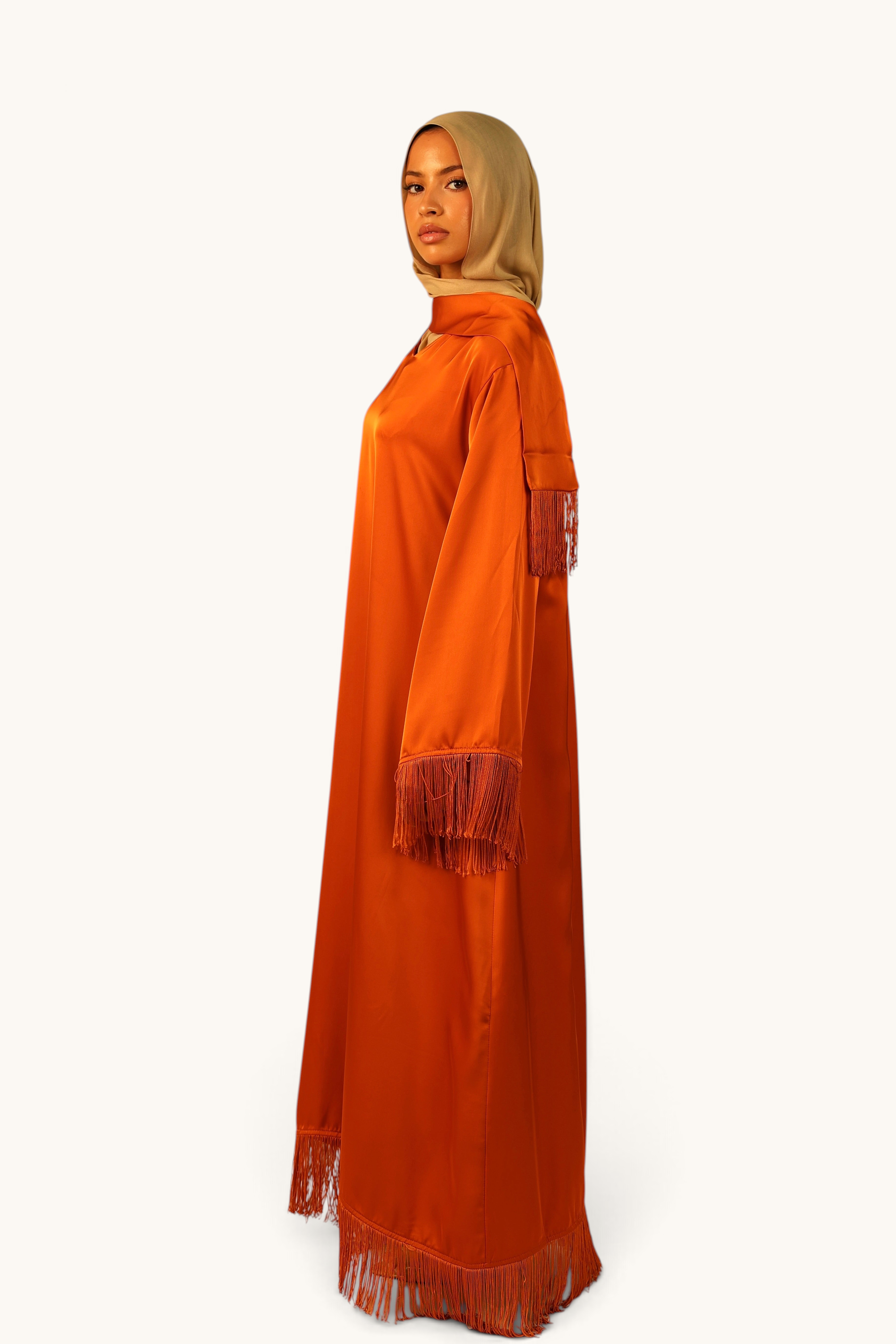 LOSYANA Barcelona Satin-Kleid in Papaya mit Fransen an Ärmeln und Saum, getragen von einem Model mit beigem Hijab.