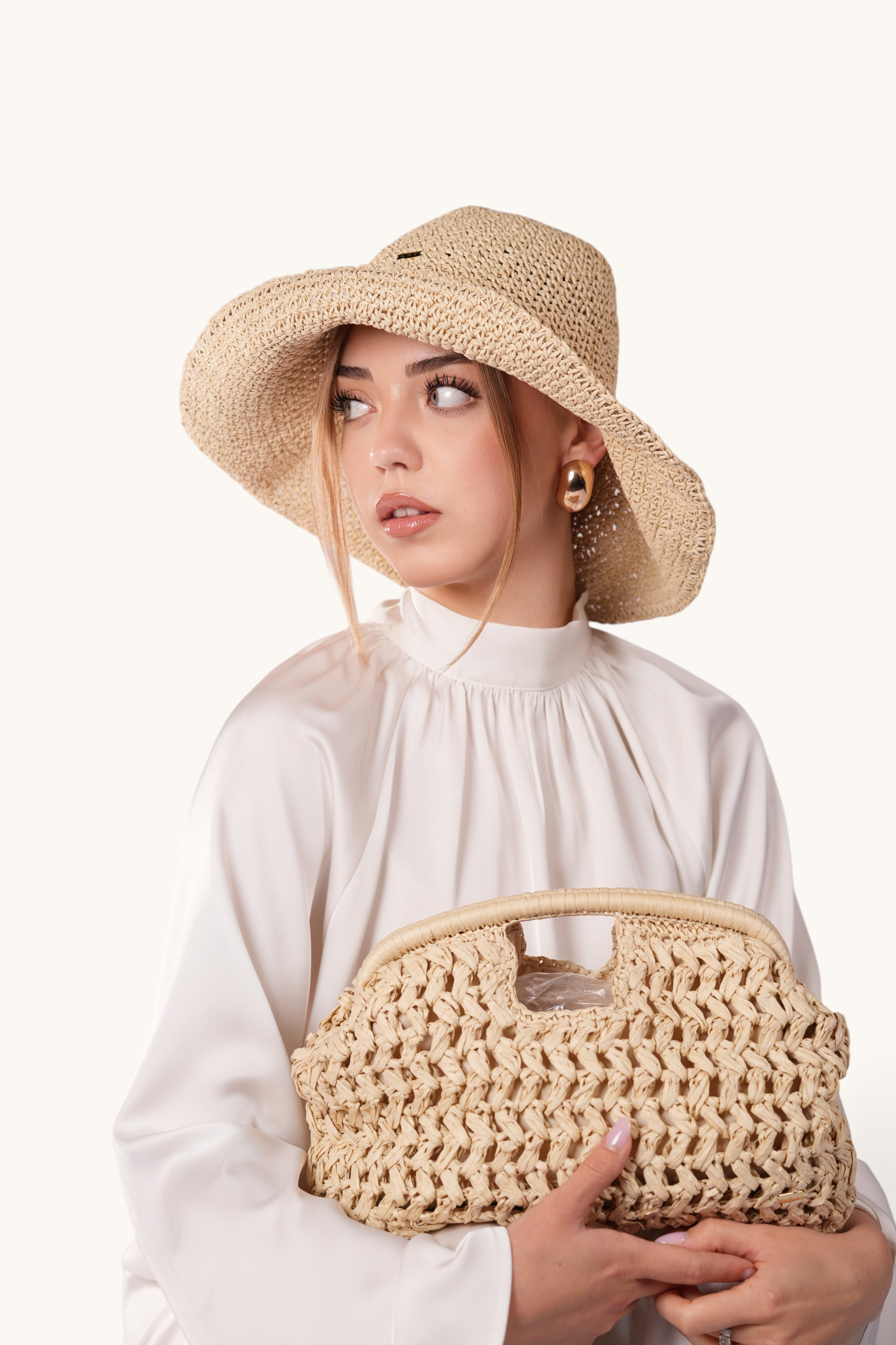 LOSYANA beige handmade straw hat with adjustable brim worn by a model holding a matching woven bag