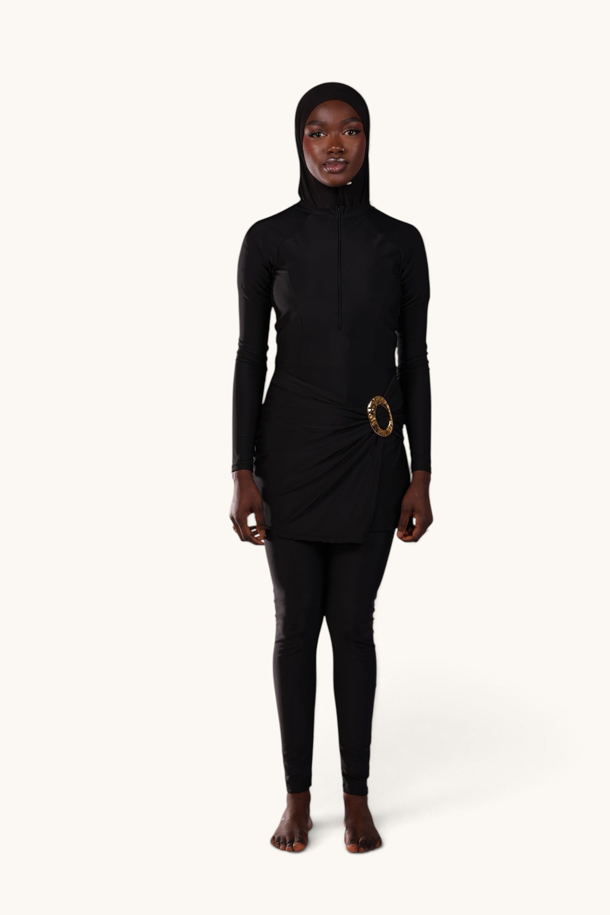Model wearing a black LOSYANA Costa Blanca burkini with a gold hip detail, long-sleeve top, leggings, and swim cap.