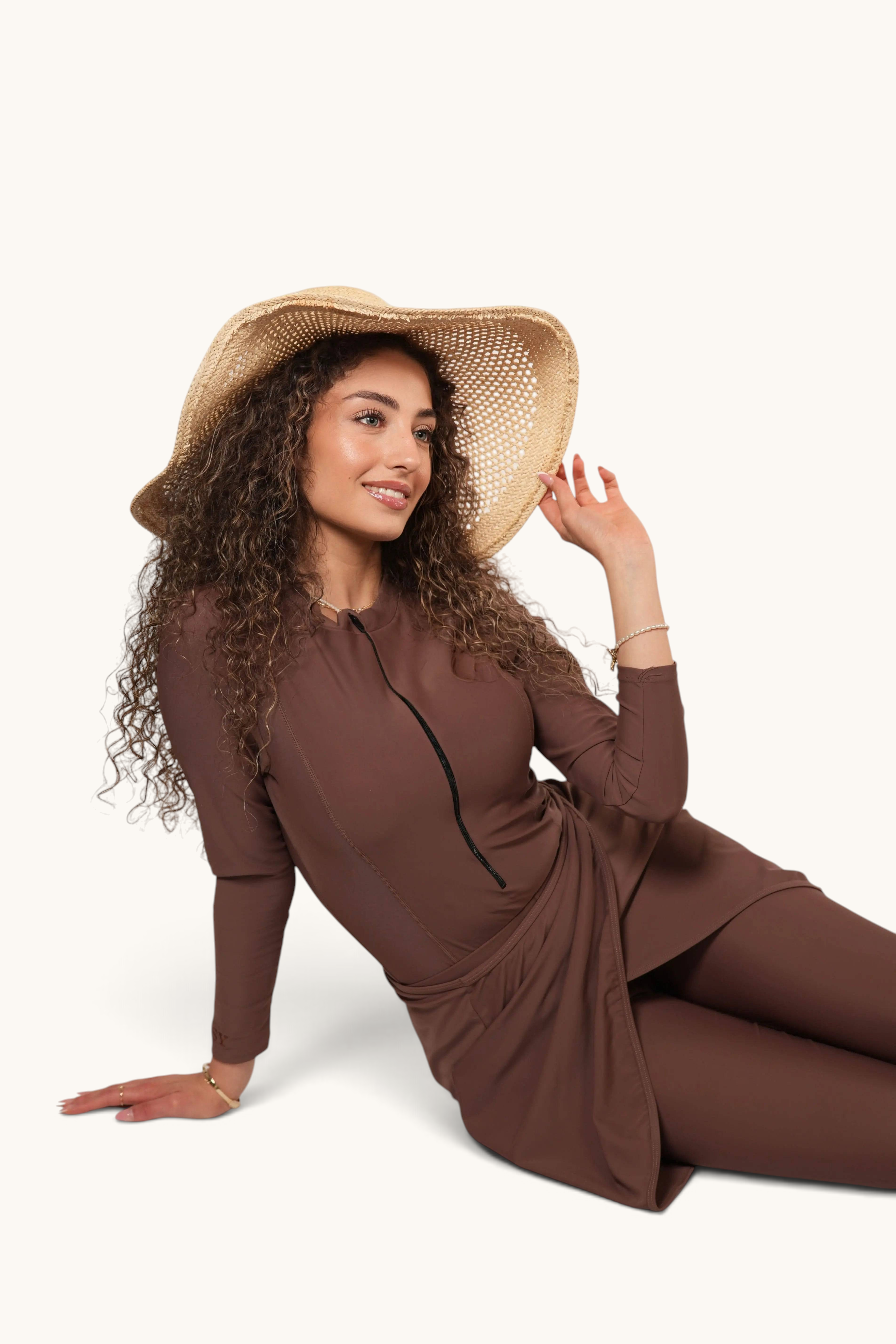 LOSYANA Costa Mare three-piece brown burkini with long sleeves and a straw hat worn by a curly-haired model