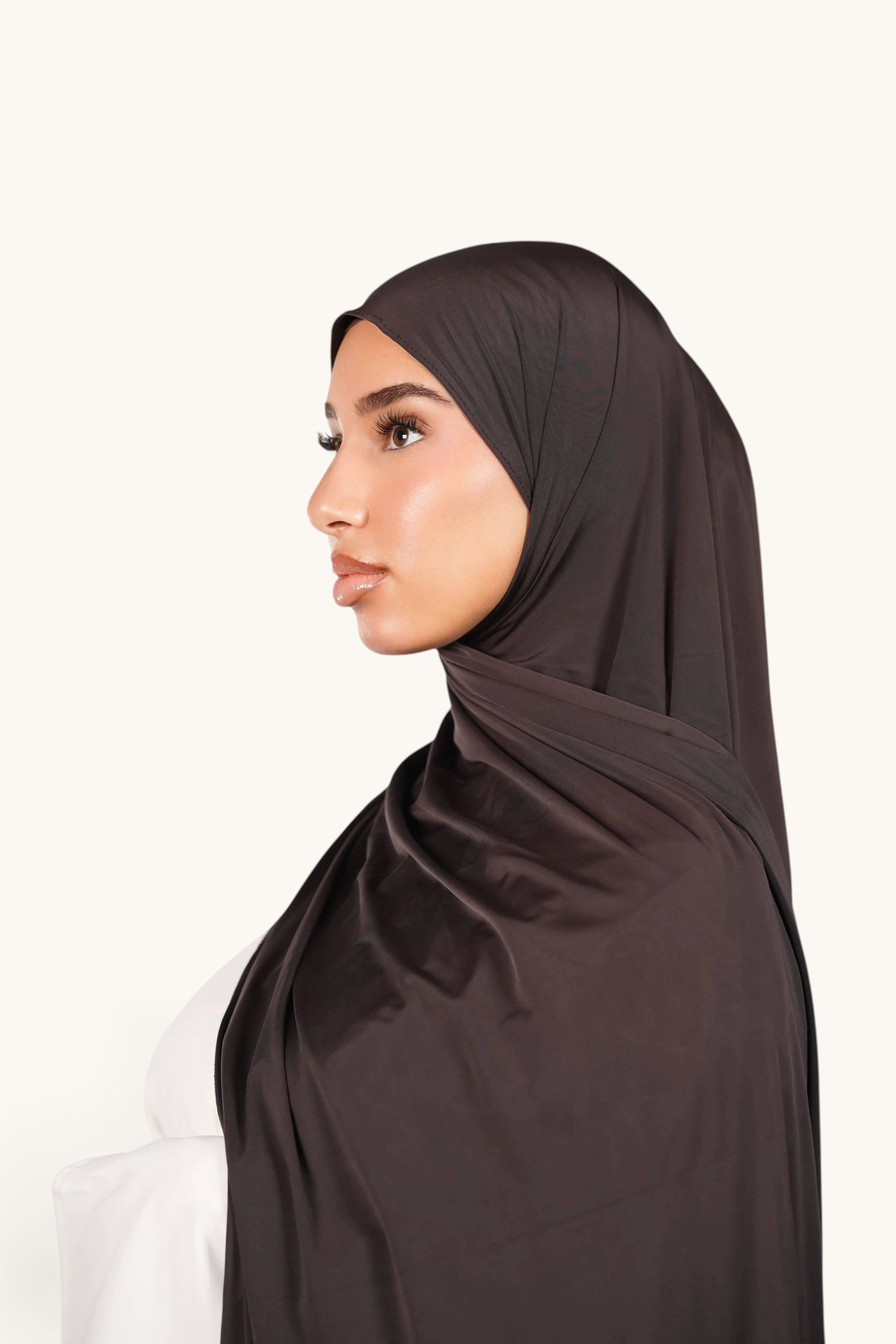 Model wearing a deep brown LOSYANA Liquid Jersey hijab with a subtle satin sheen, side profile view.