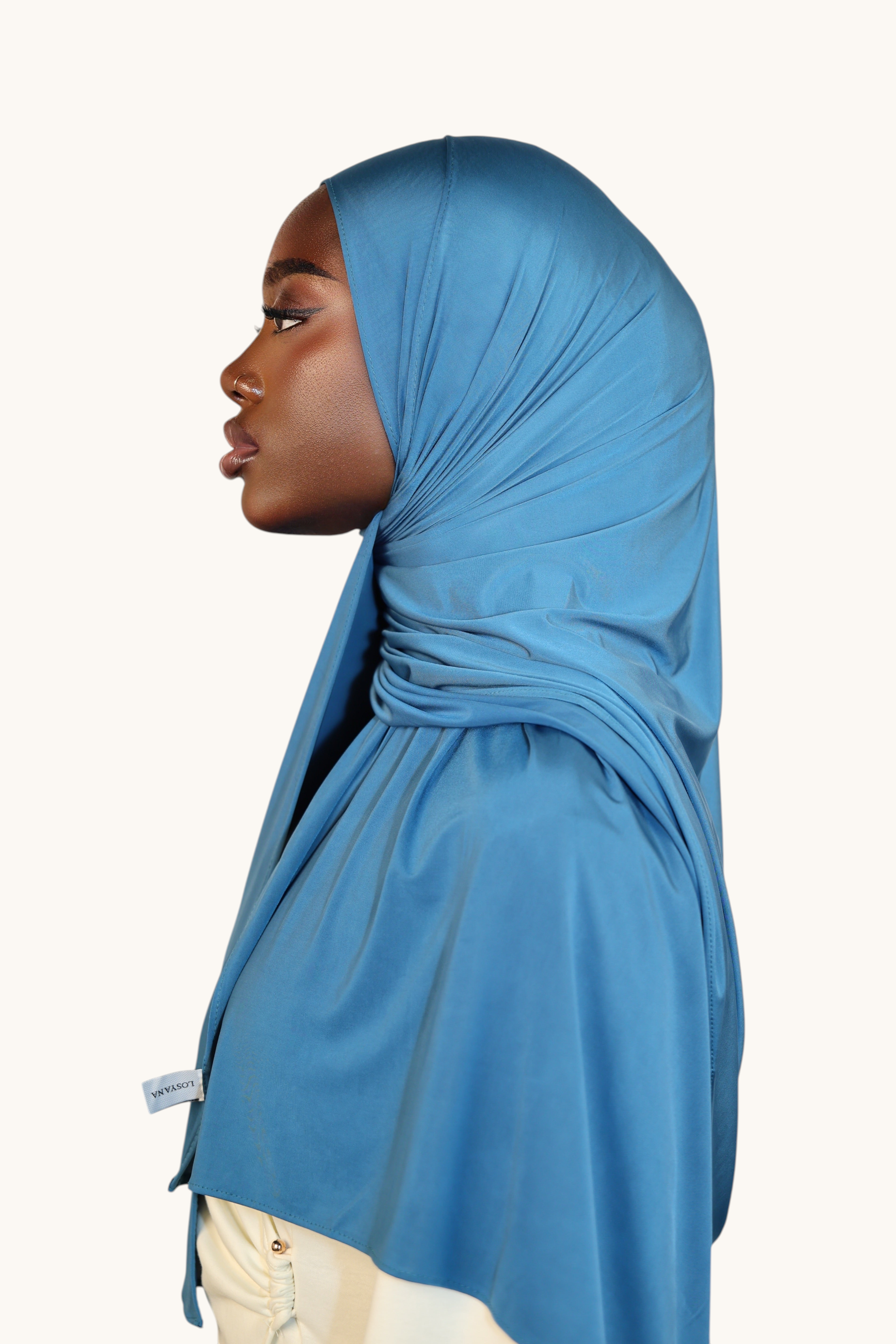 Model wearing a LOSYANA ice blue liquid jersey hijab with a subtle satin sheen, shown in profile view.
