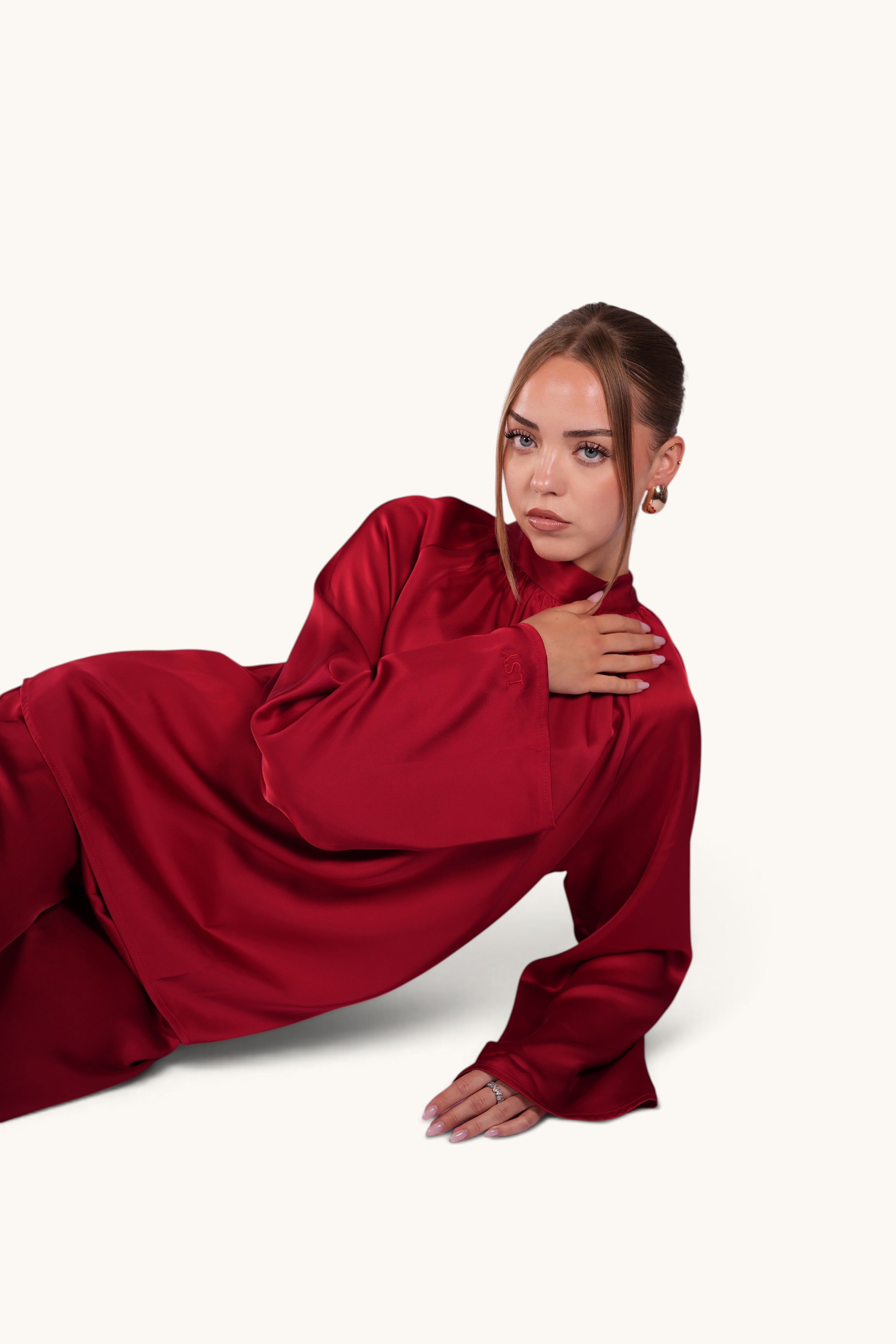 Model wearing LOSYANA La Palma red satin two-piece set with high collar and long sleeves, posing on white background.