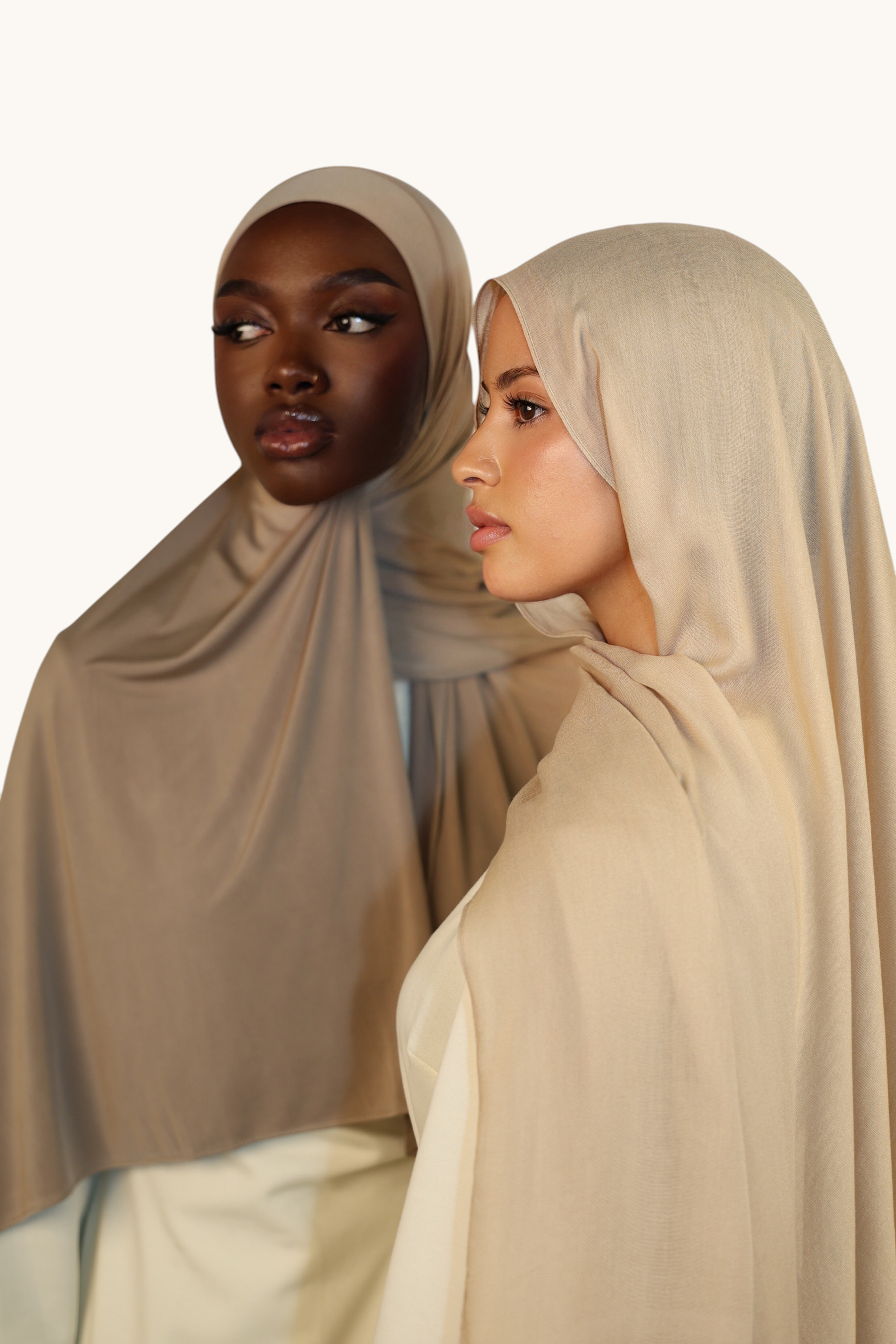 Two models wearing LOSYANA oat-colored liquid jersey hijabs with a soft, elegant sheen and breathable fabric.