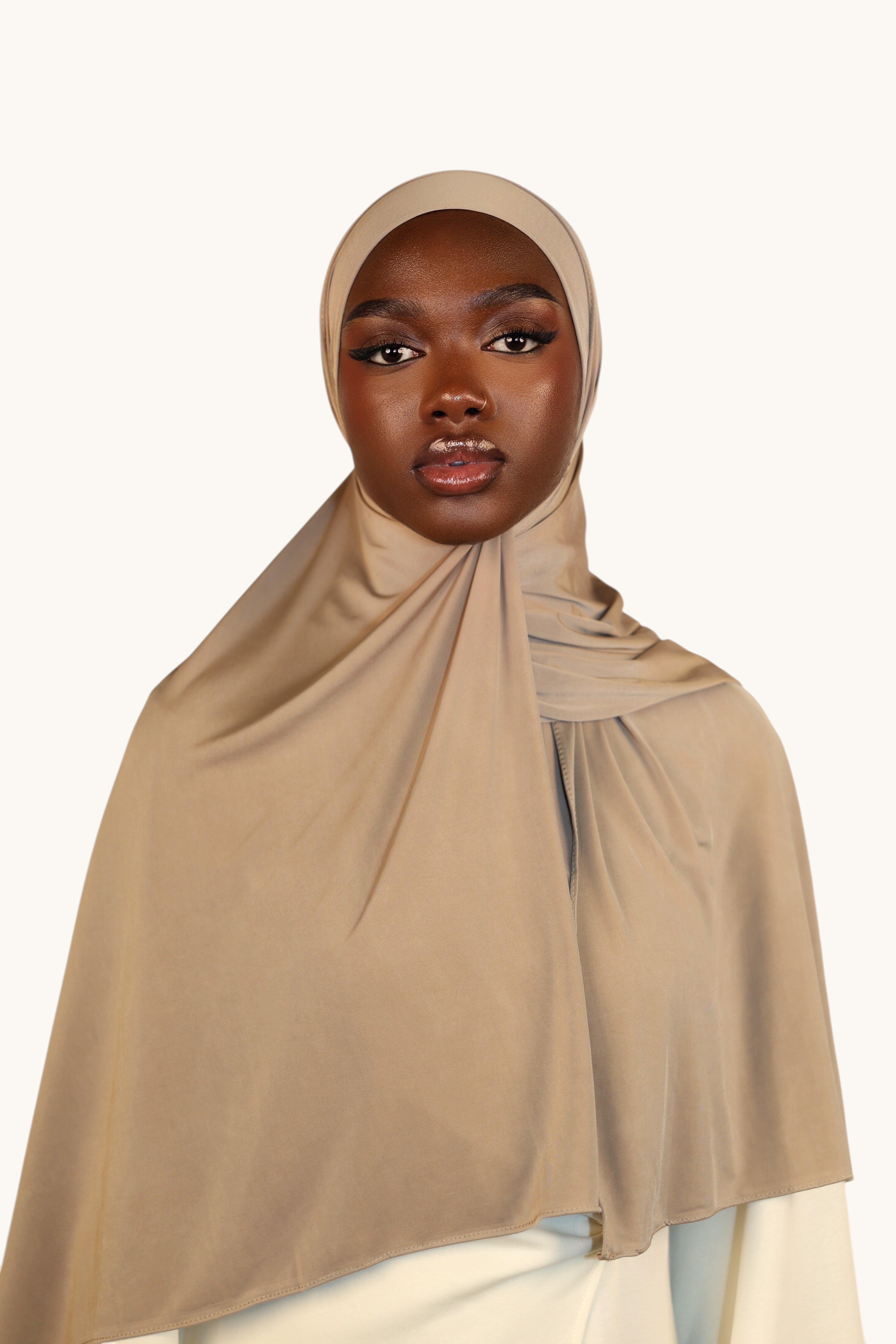 Model wearing a LOSYANA Liquid Jersey hijab in oat, featuring a lightweight, breathable, and subtly glossy fabric.