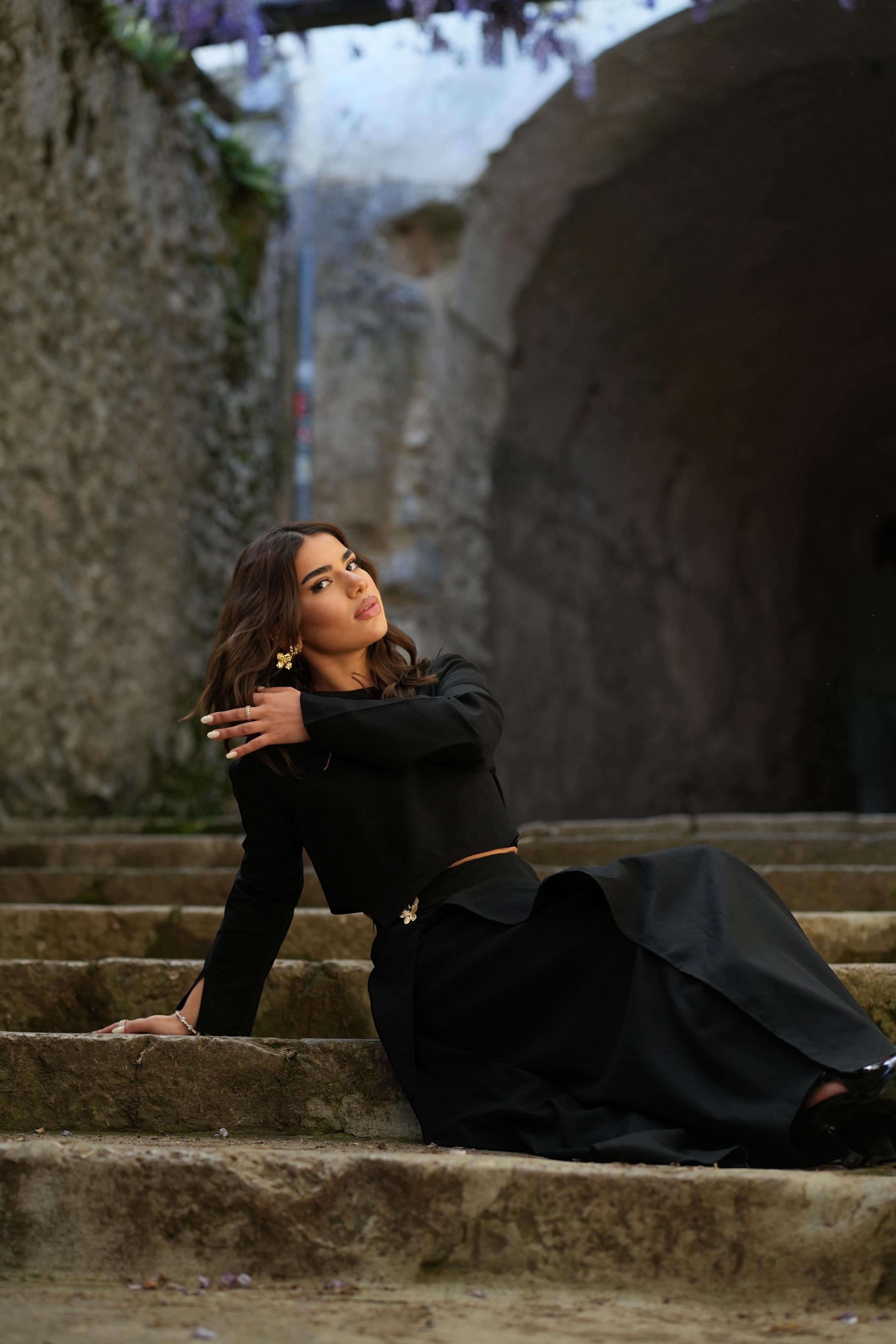 Model wearing a black LOSYANA Mediterrance Serenity Set in linen-cotton blend, sitting on stone steps outdoors.