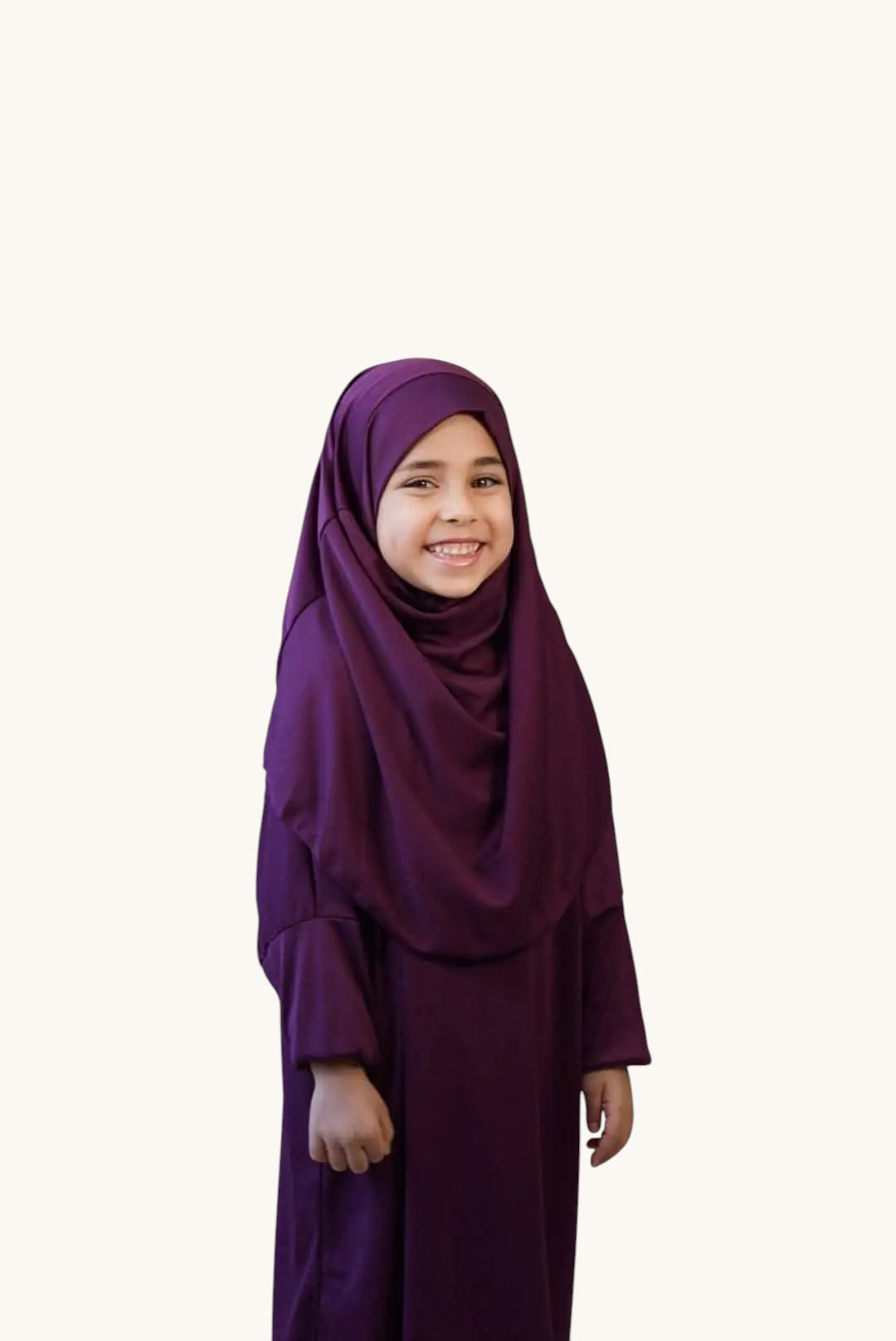 A young girl smiling while wearing a comfortable purple LOSYANA jersey prayer dress with an attached hijab.