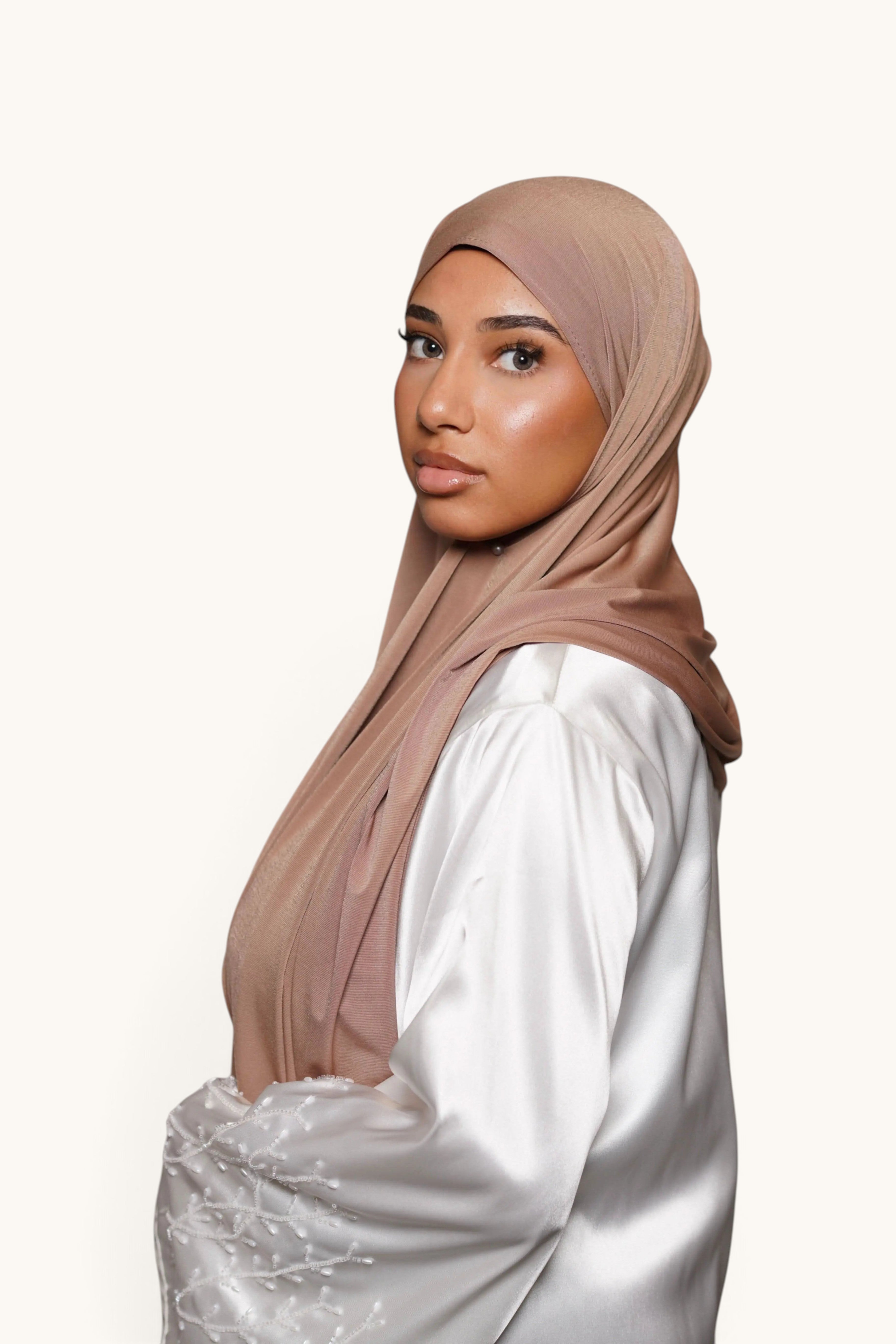 Model wearing a LOSYANA sand-colored satin jersey hijab, featuring a smooth, opaque, and non-slip fabric drape.