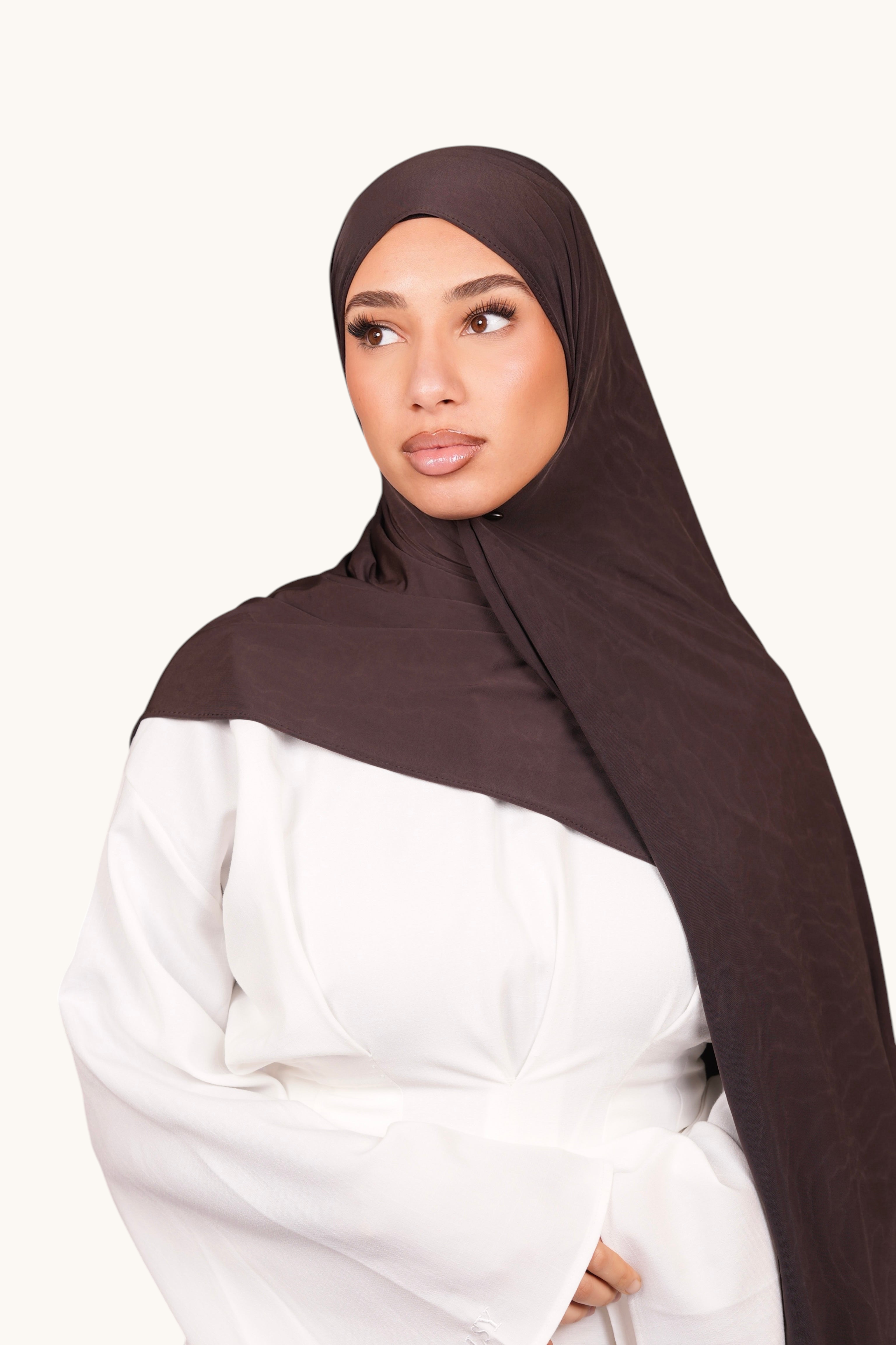 Model wearing a LOSYANA smokey chocolate liquid jersey hijab with a subtle sheen, styled over a white top.