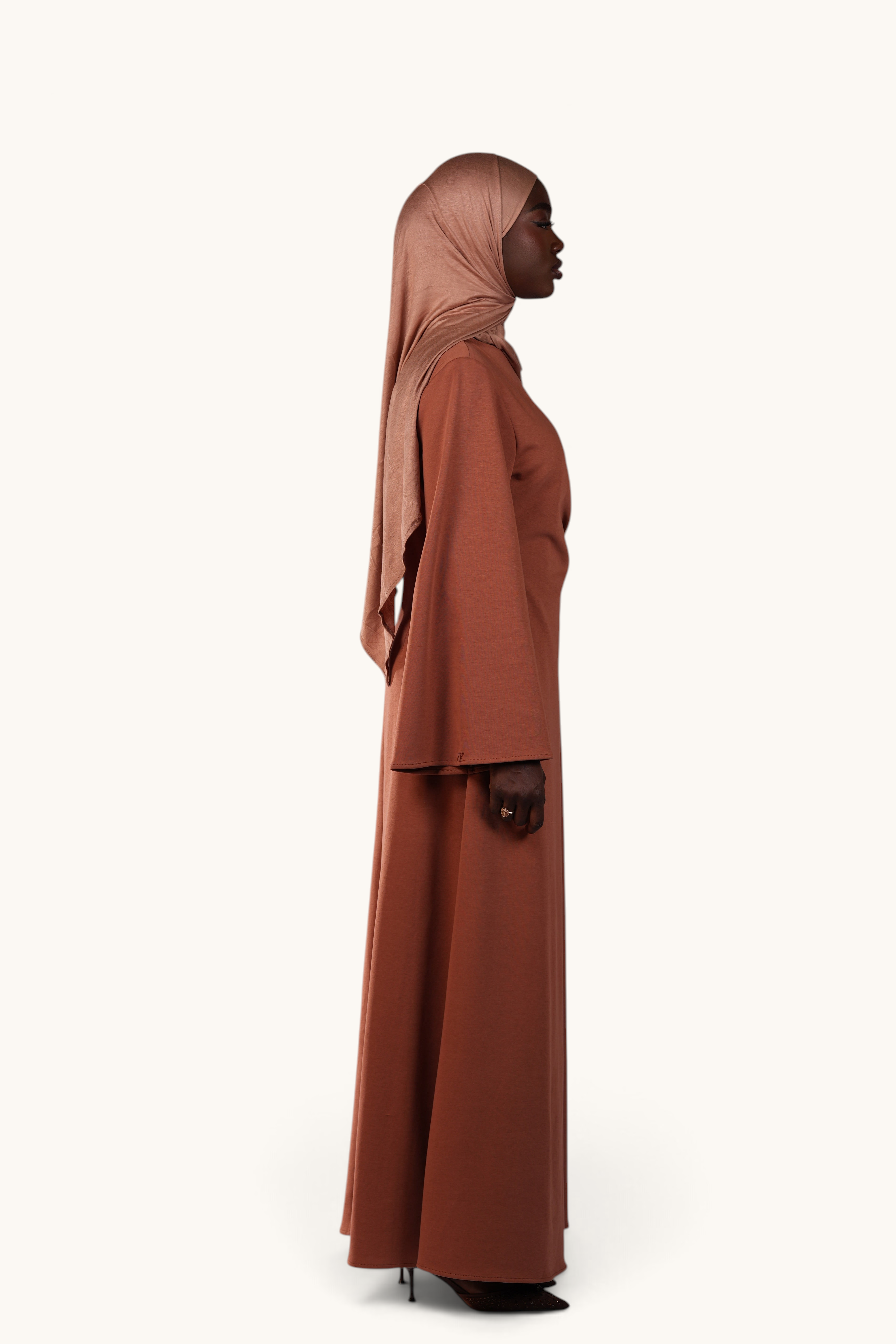 LOSYANA Valencia terracotta maxi dress with trumpet sleeves and gold detail worn by a model in a side profile view