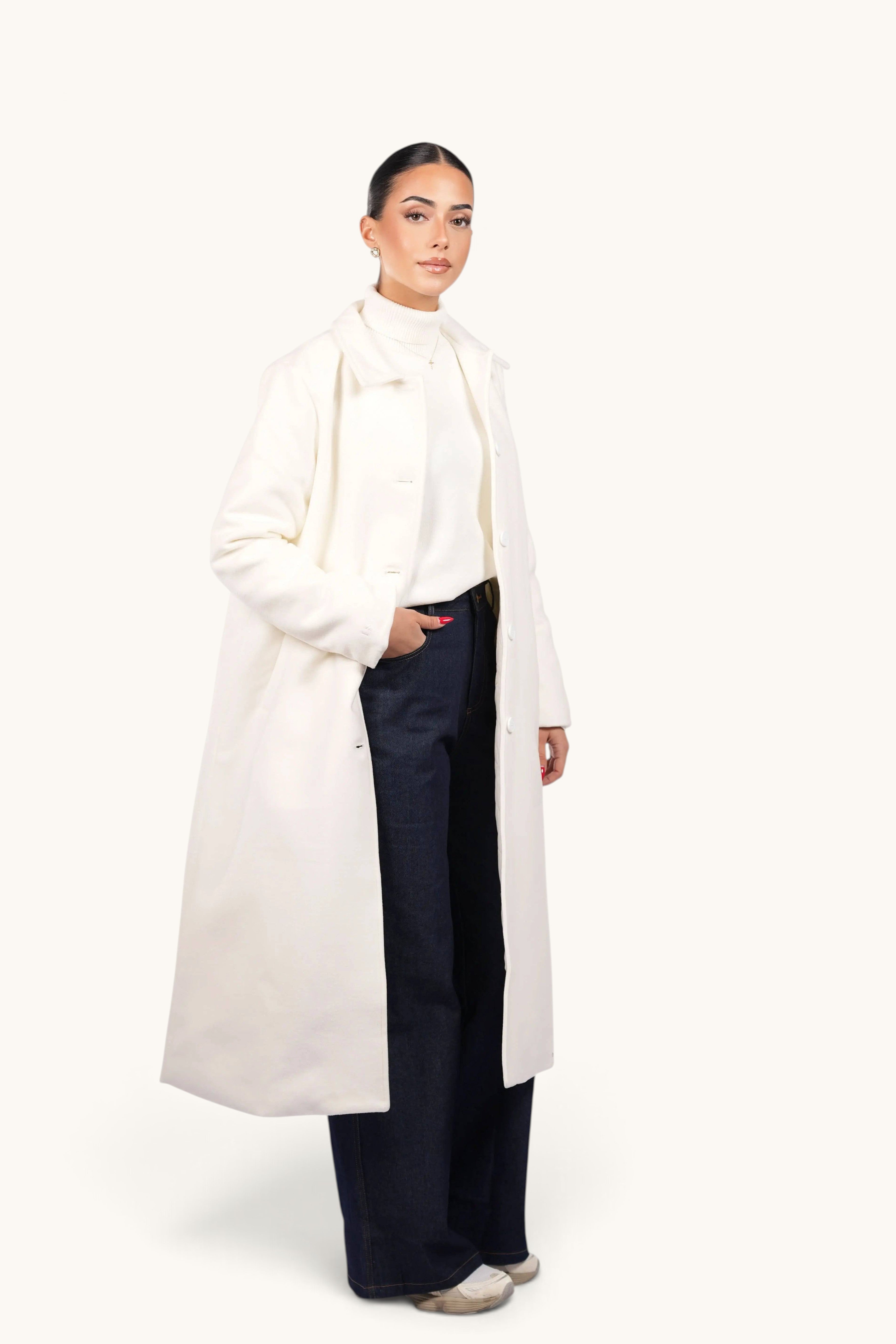 Model wearing a LOSYANA white Vienna coat over a white turtleneck and dark blue jeans against a plain background