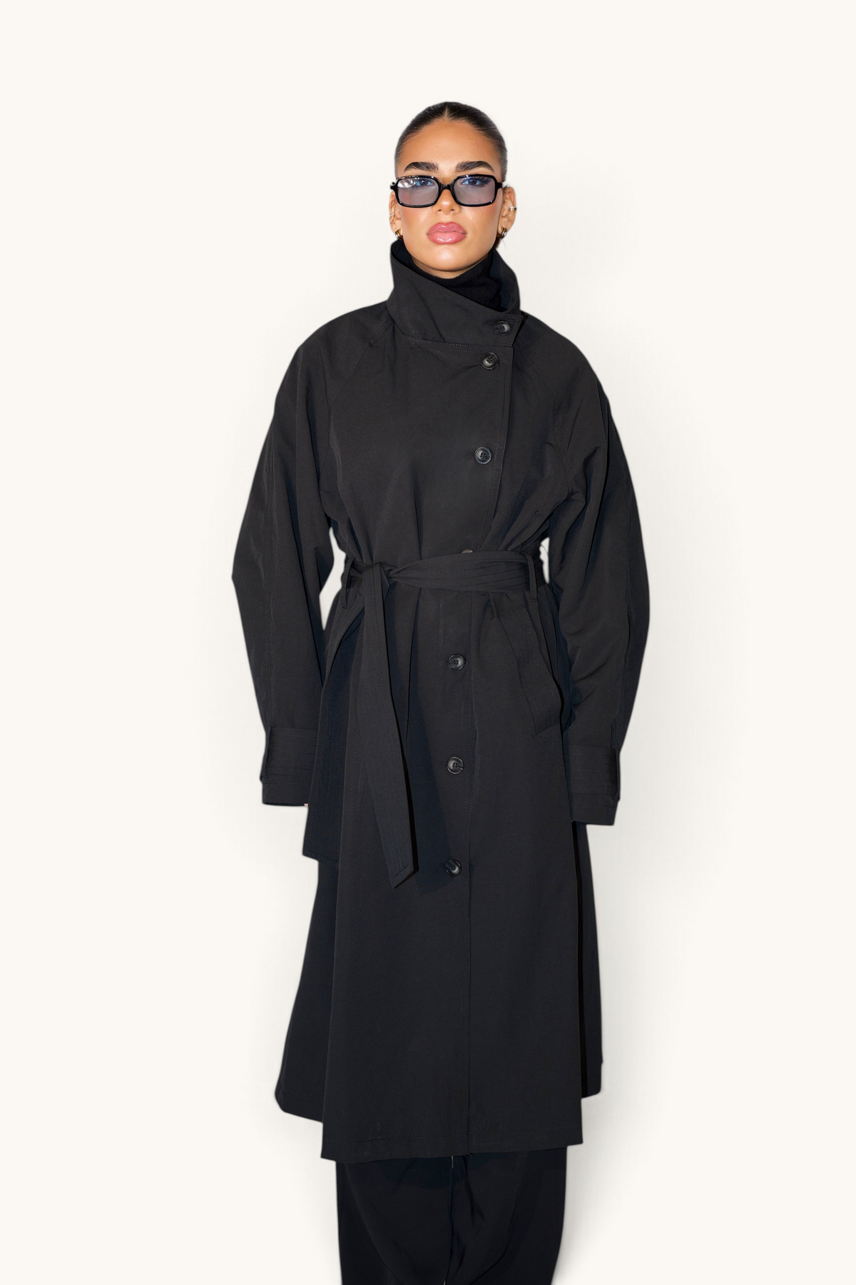 Langer schwarzer Trenchcoat von LOSYANA, eleganter Mantel mit Gürtel und klassischen Revers, auf einem Kleiderbügel hängend