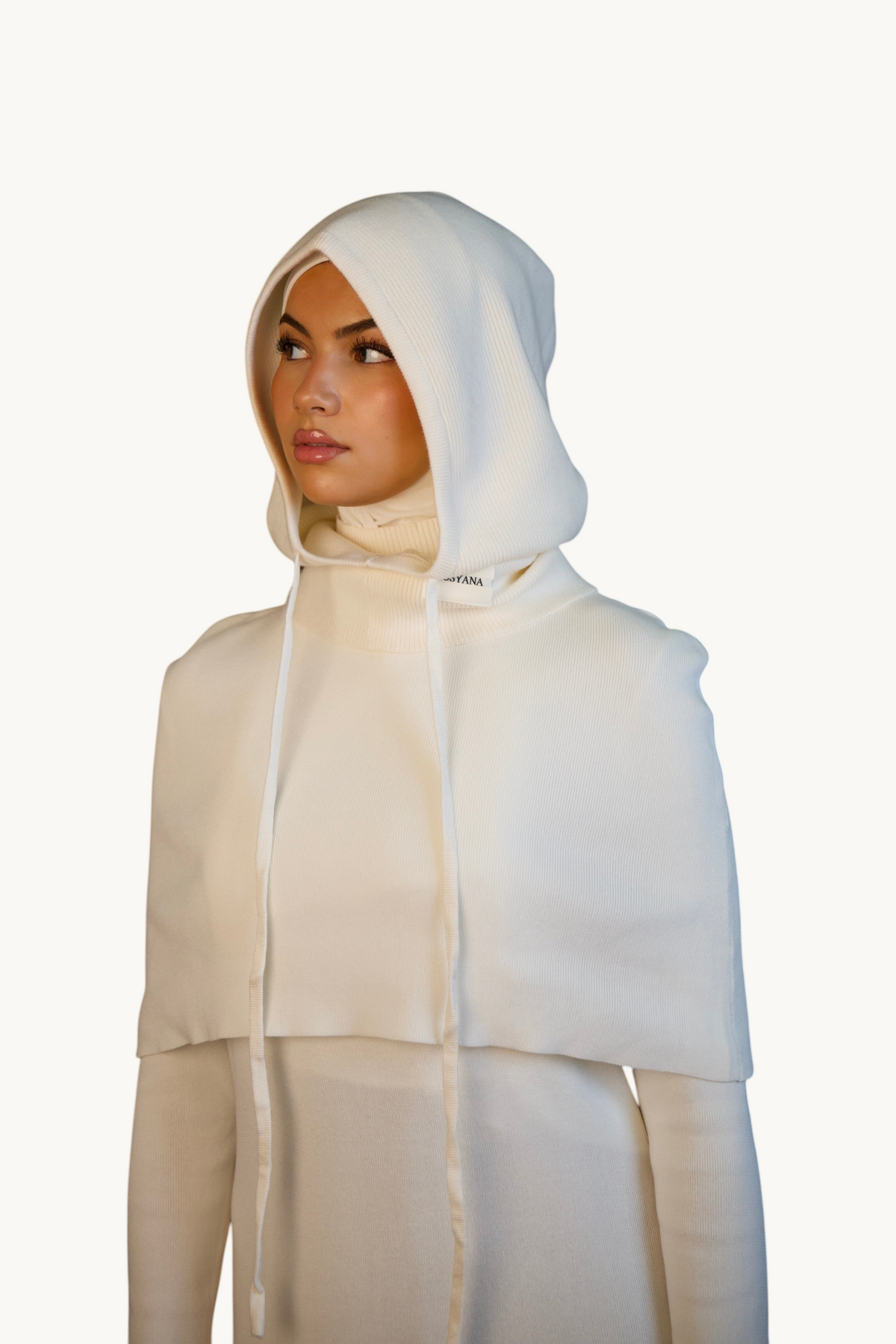 LOSYANA Balaclava in Creme aus weichem Strick mit Kapuze, Kordelzug und entspannter Passform vor braunem Hintergrund