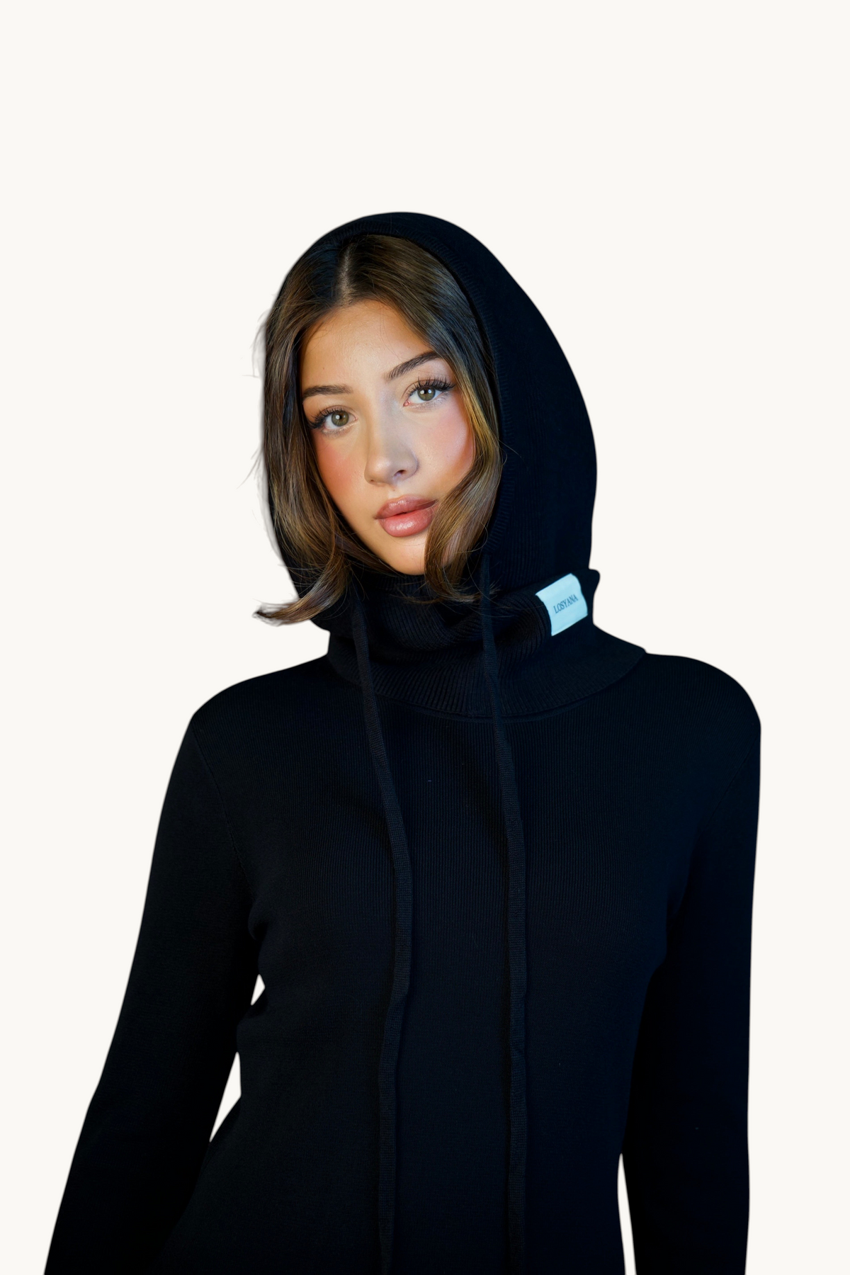 LOSYANA Balaclava in Schwarz aus weichem Strick mit Kapuze, Kordelzug und Logo-Label, getragen von einer Frau.