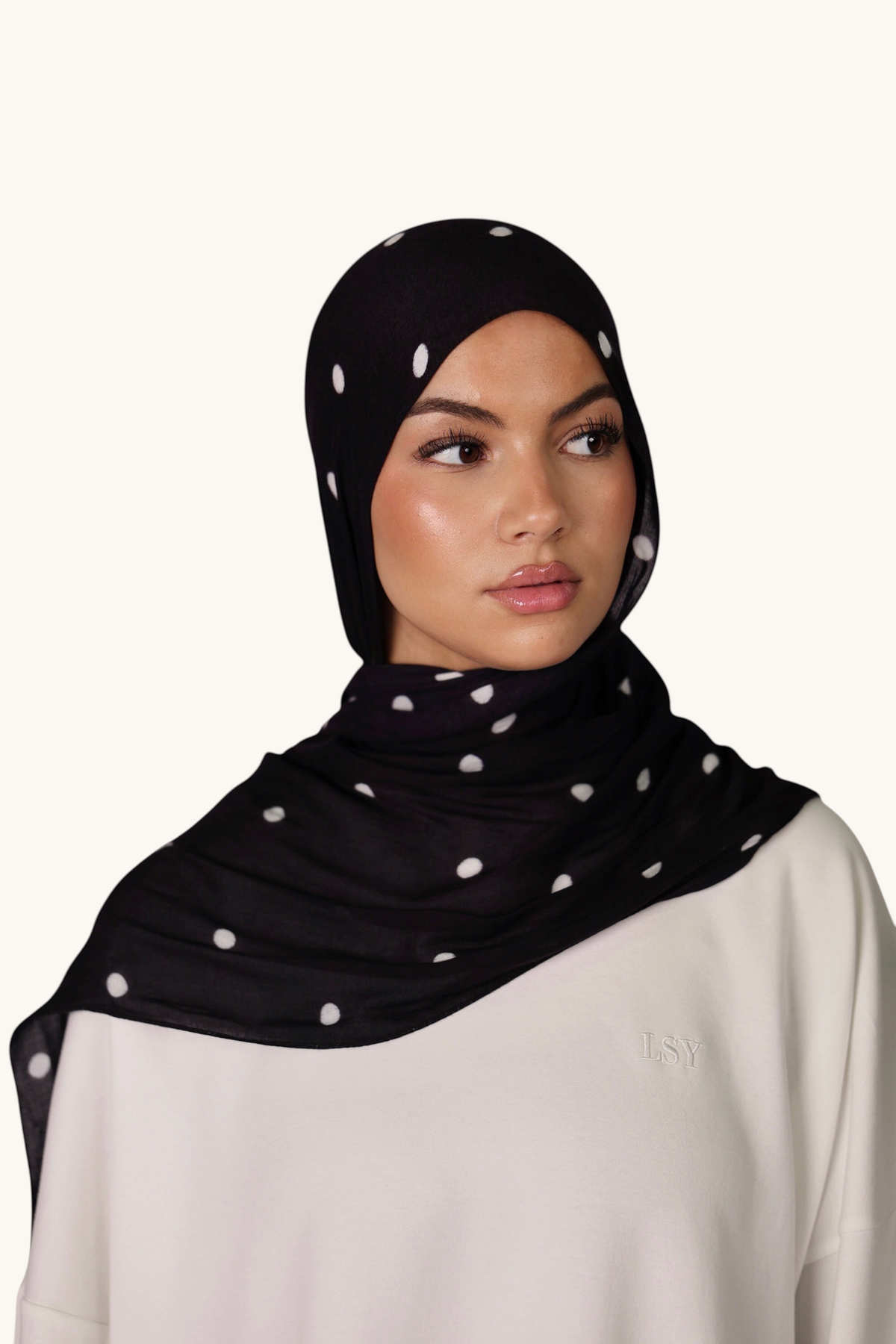LOSYANA Hijab aus schwarzem Modal mit weißen Velour-Punkten, getragen von einem Model vor hellem Hintergrund.