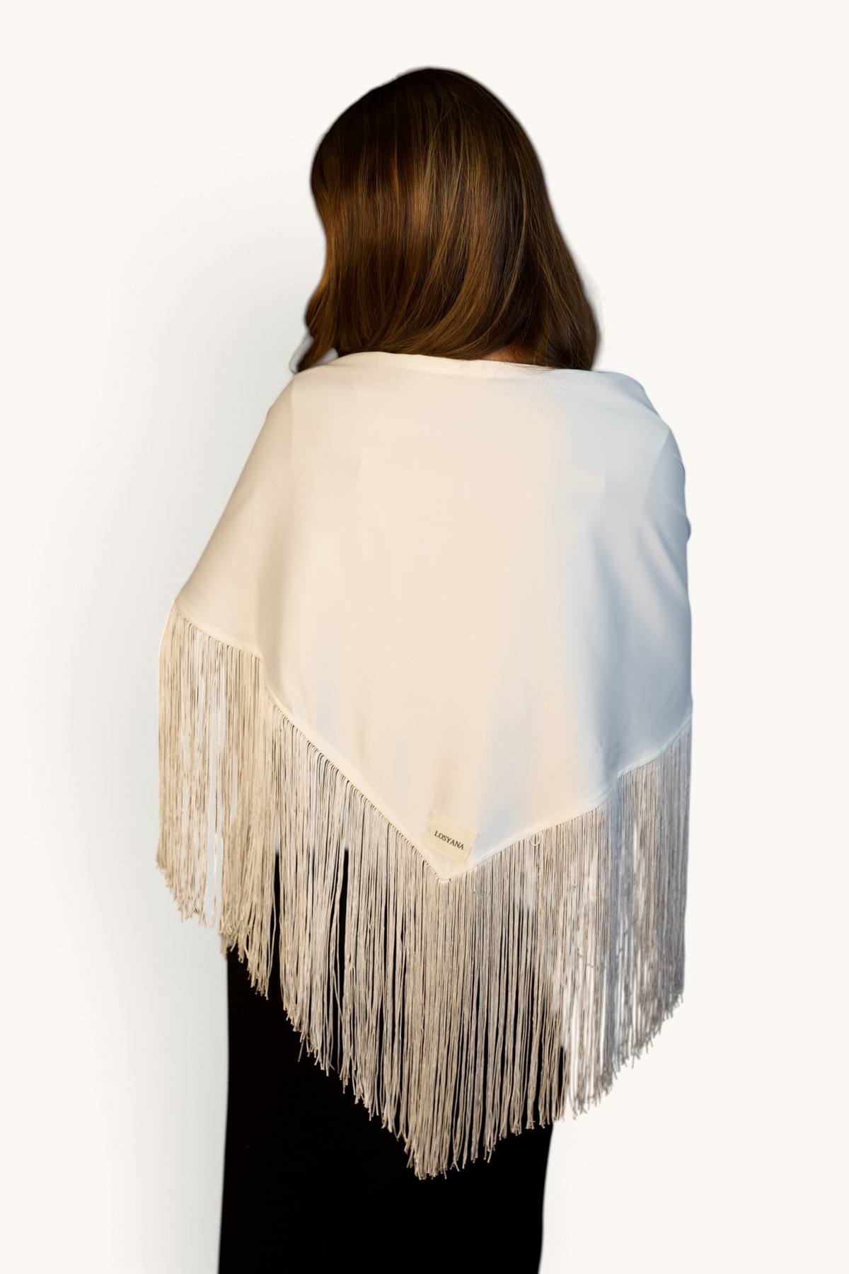 LOSYANA weißes Satin-Cape mit langen Fransen am Saum, getragen von einem Model vor braunem Hintergrund