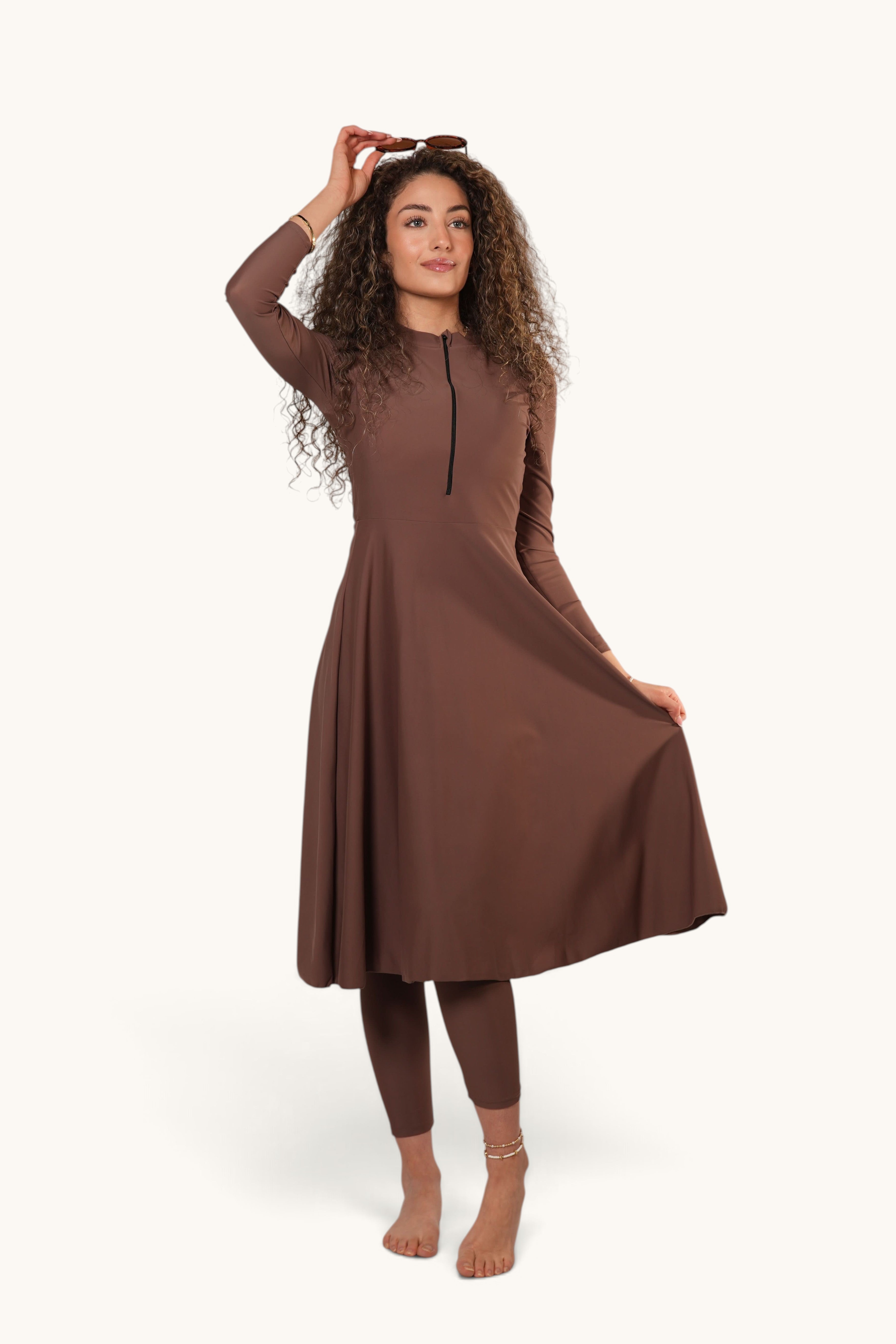 Model wearing a brown LOSYANA Azzurra long-sleeve burkini set with a zip-front tunic and matching leggings.