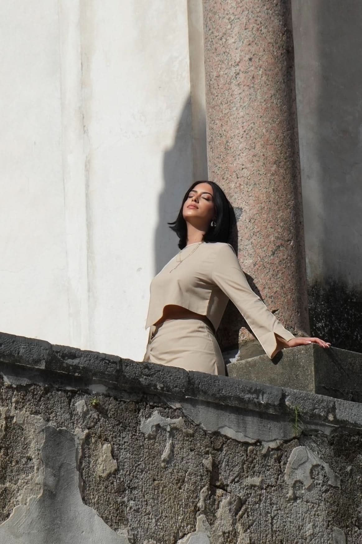 Model wearing a beige LOSYANA Mediterrance Serenity set in linen-cotton blend, posing against a stone pillar outdoors.