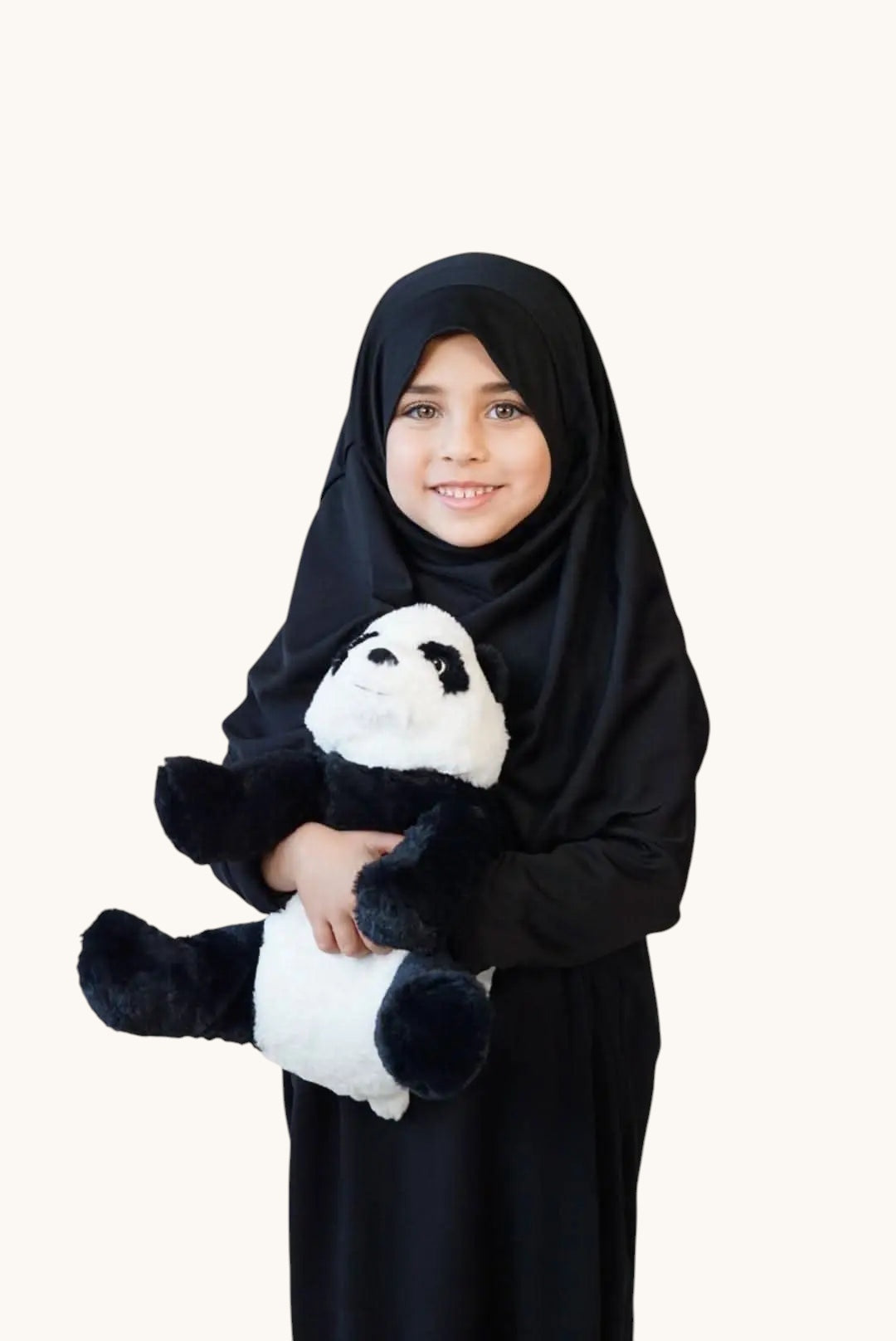 Young girl wearing a black LOSYANA jersey prayer dress and hijab, smiling while holding a plush panda toy.