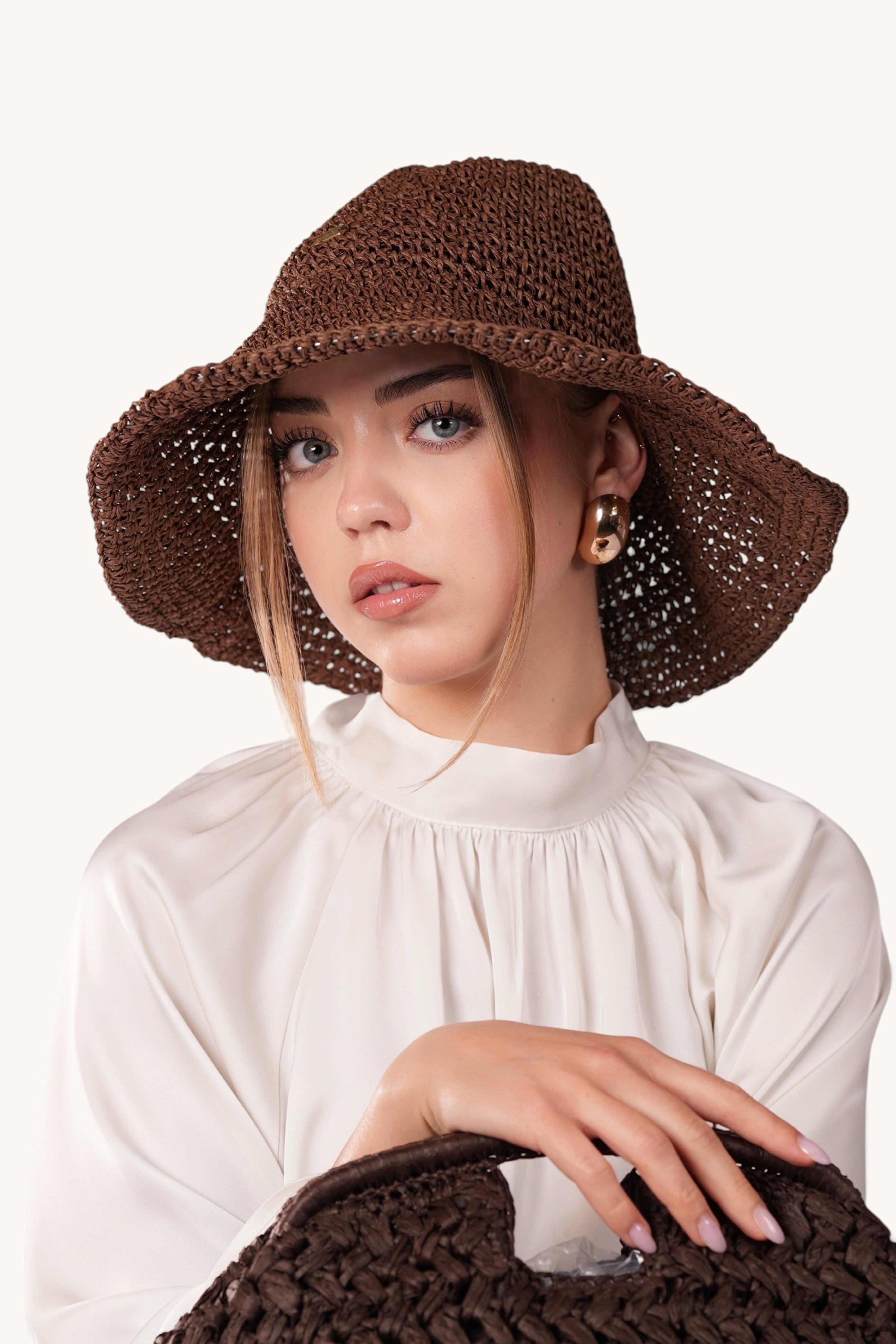 A woman wearing a LOSYANA espresso brown handcrafted straw hat with a flexible brim, paired with a matching bag.
