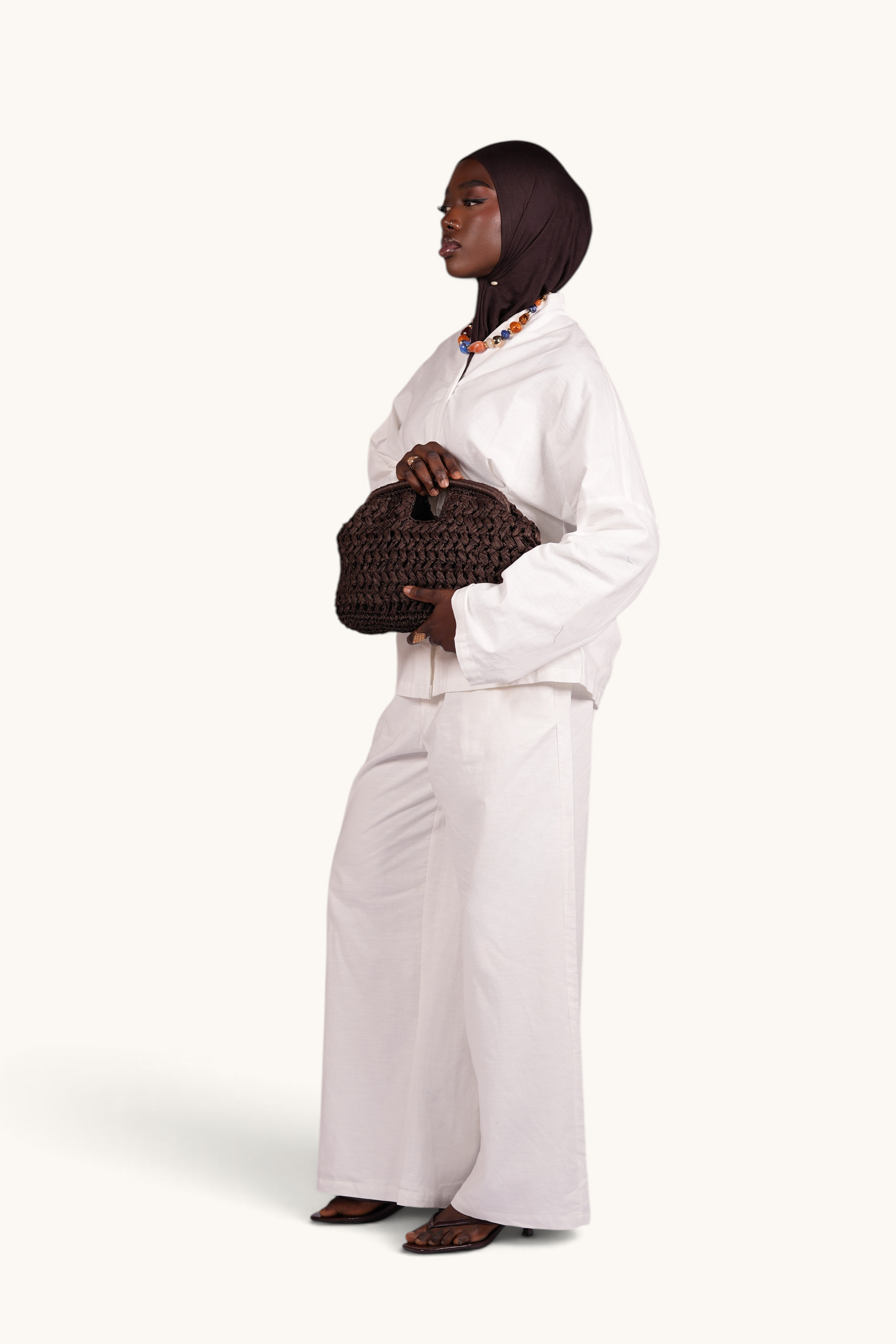 LOSYANA espresso brown handmade woven straw bag held by a model wearing a white linen outfit and a dark headscarf