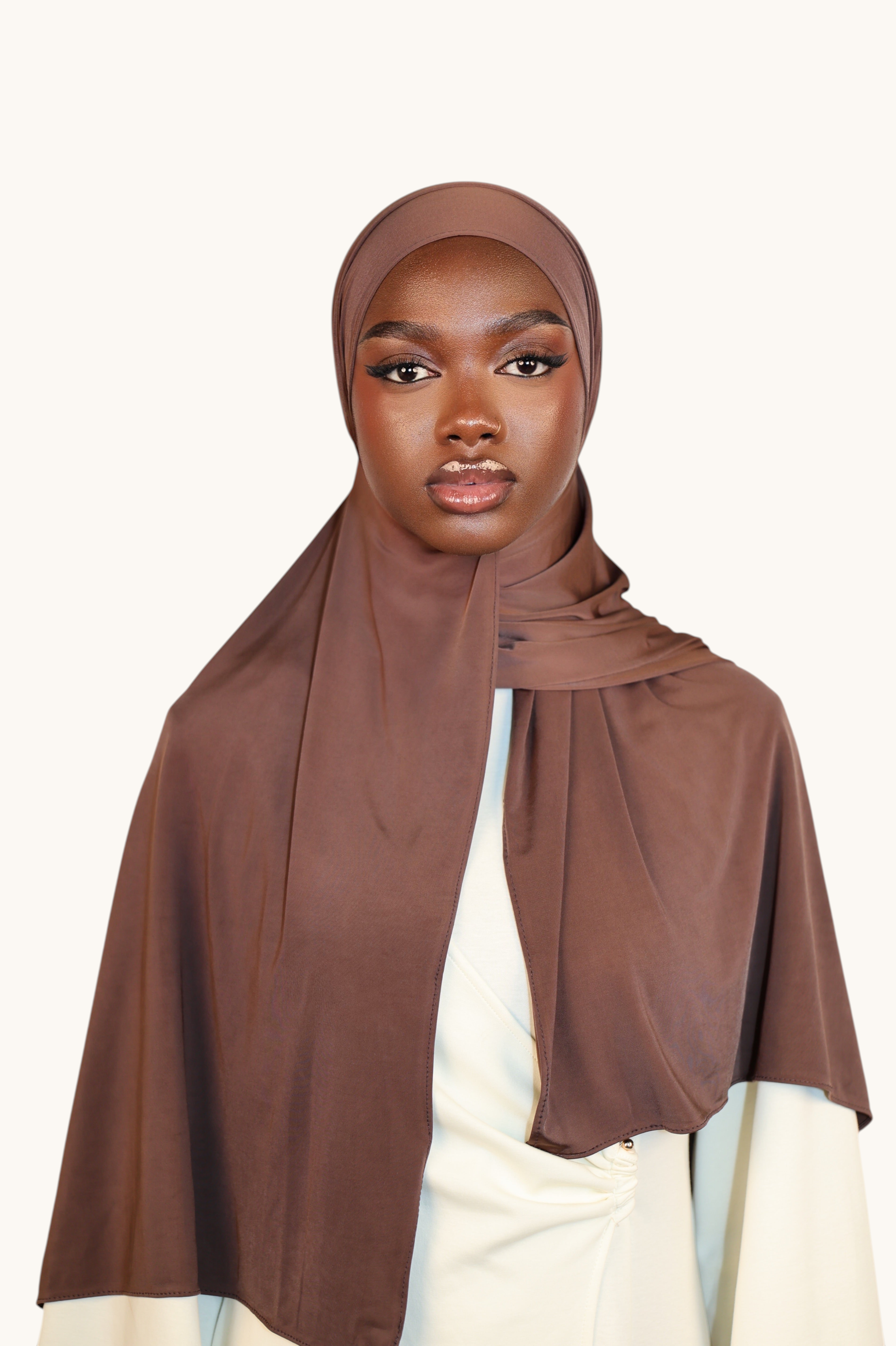Model wearing a LOSYANA Liquid Jersey hijab in burnt sugar, a lightweight, slightly glossy brown fabric.