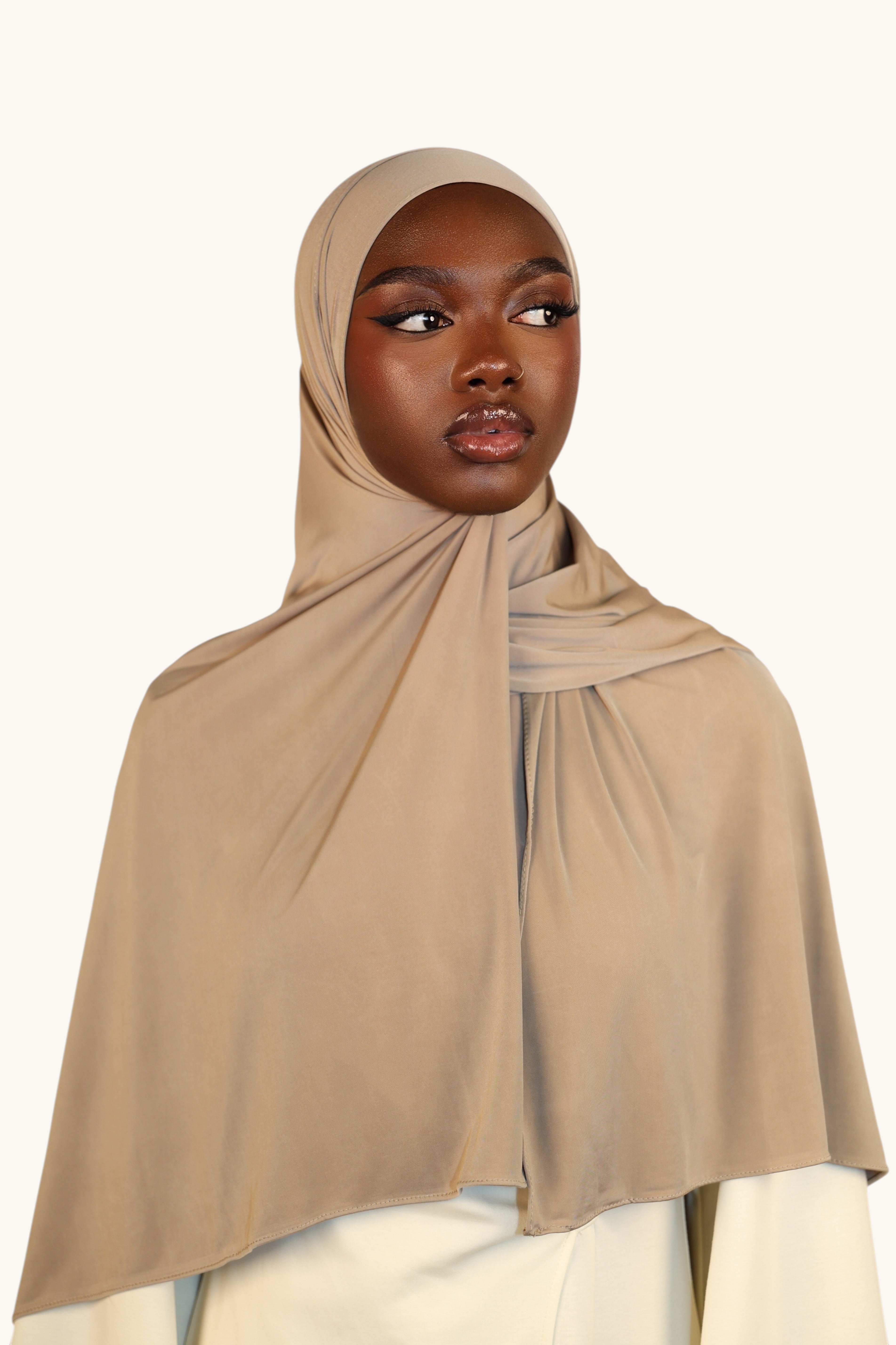 Model wearing a LOSYANA Liquid Jersey hijab in oat, featuring a lightweight, slightly glossy breathable fabric.