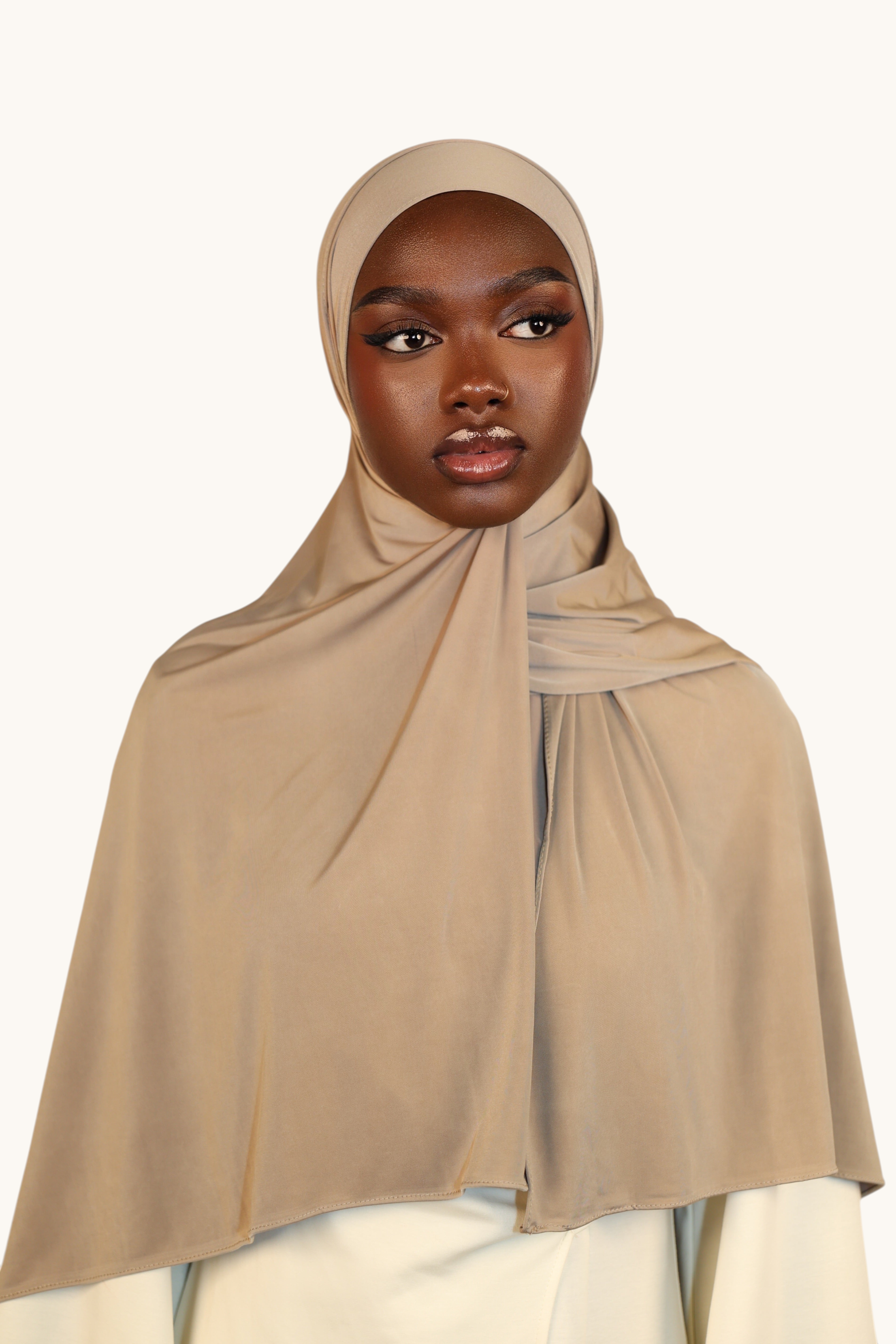 Model wearing a LOSYANA Liquid Jersey hijab in oat, featuring a lightweight, elegant, and slightly glossy fabric.