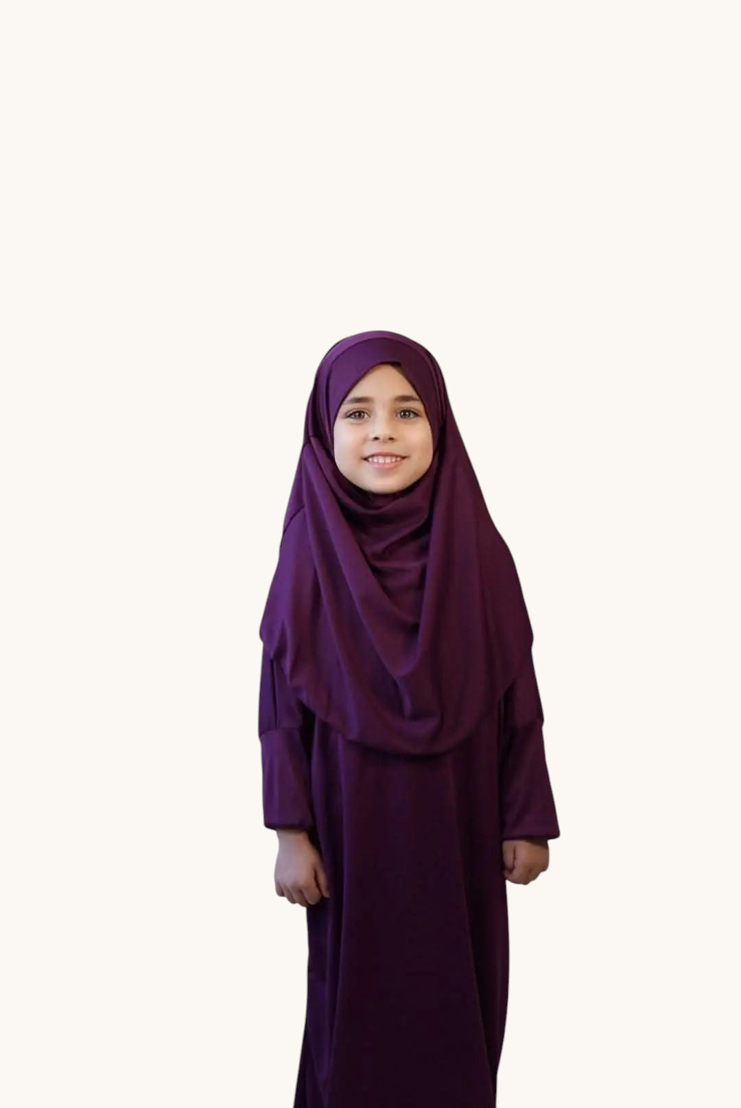 A young girl wearing a purple LOSYANA jersey prayer dress with a matching hijab, standing by a large houseplant.