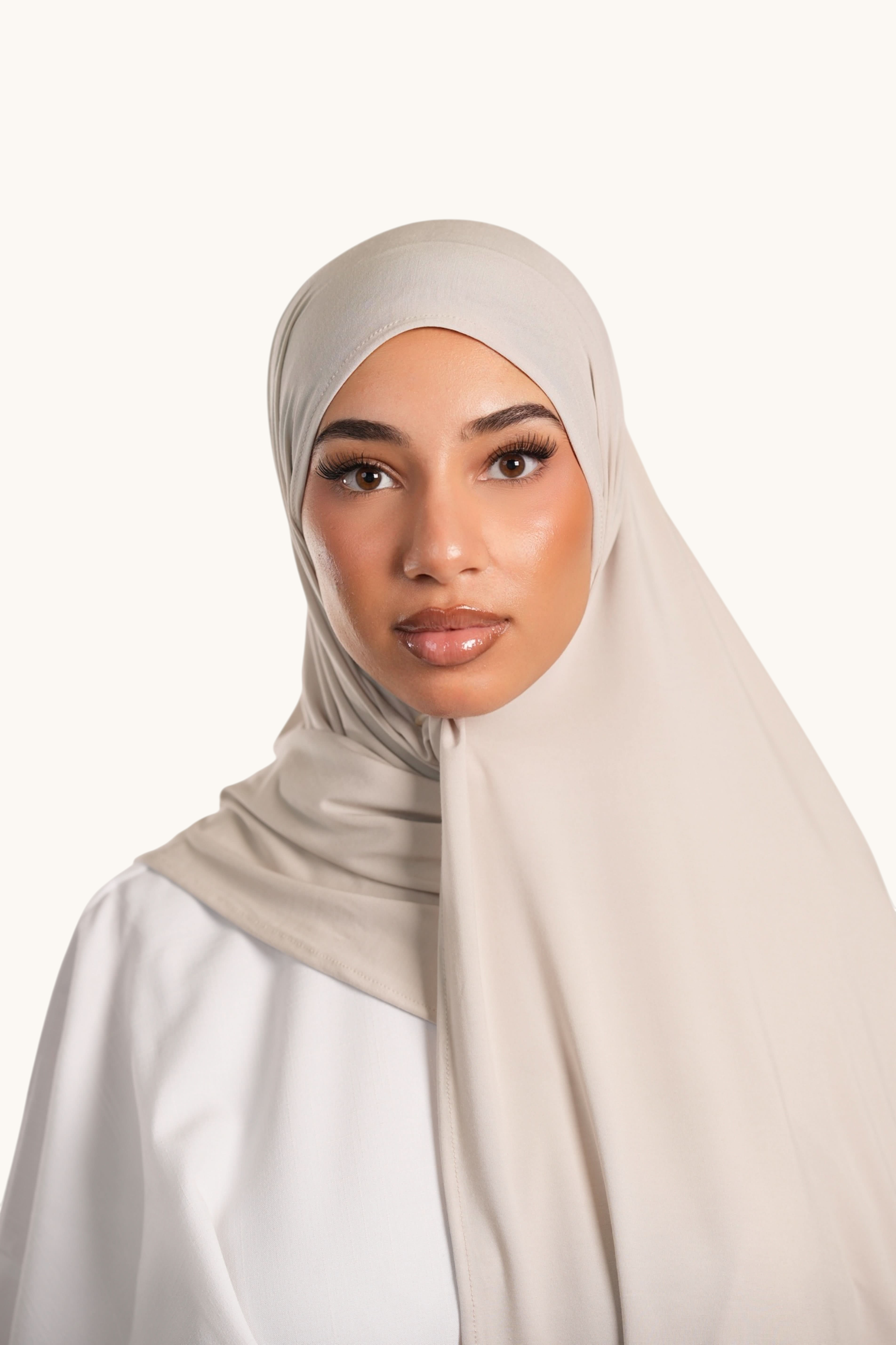 Model wearing a light beige LOSYANA Vela jersey hijab made of soft, breathable fabric in a studio setting.