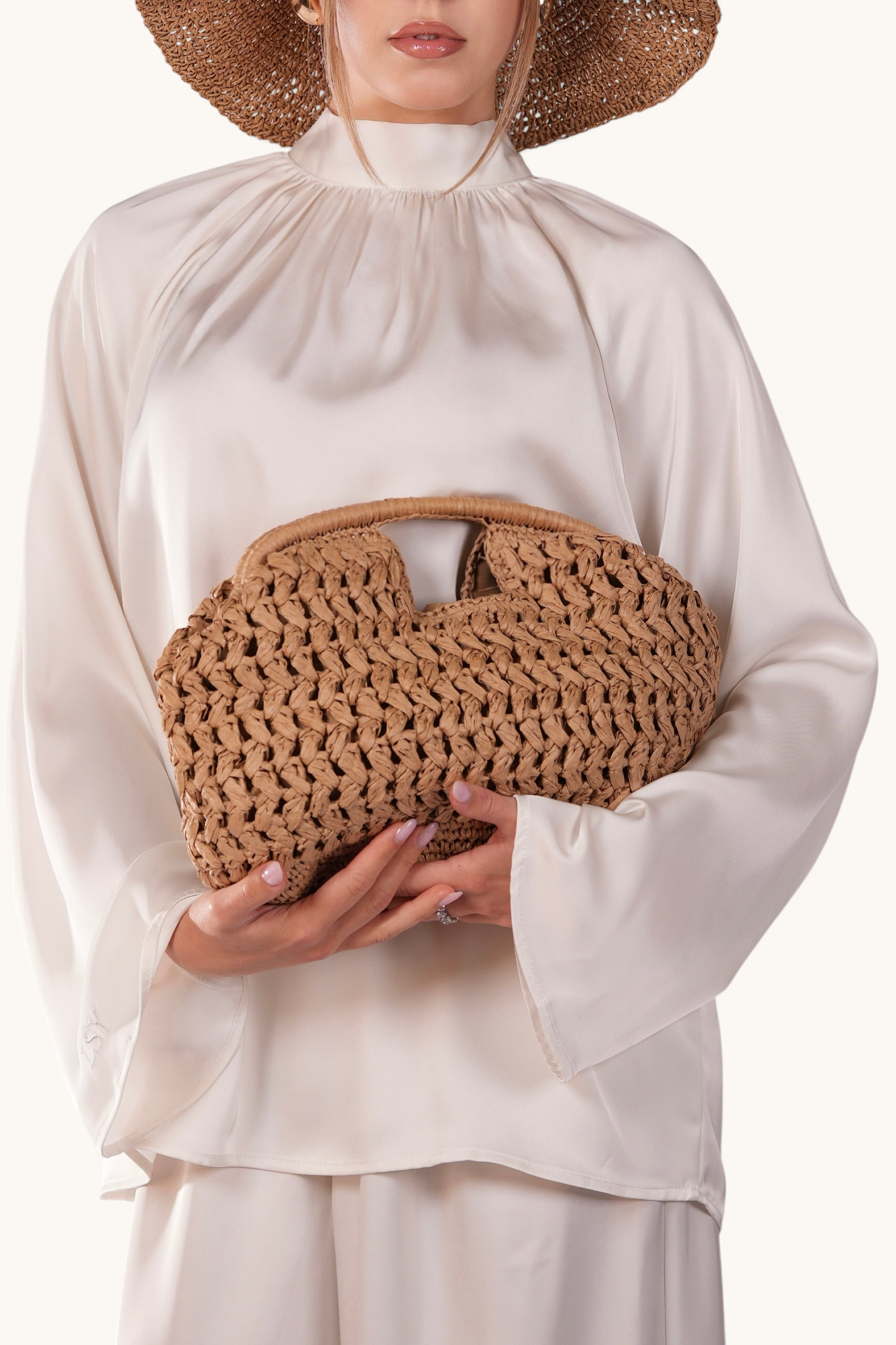 LOSYANA walnut straw woven handbag held by a model wearing a matching straw hat and cream satin blouse